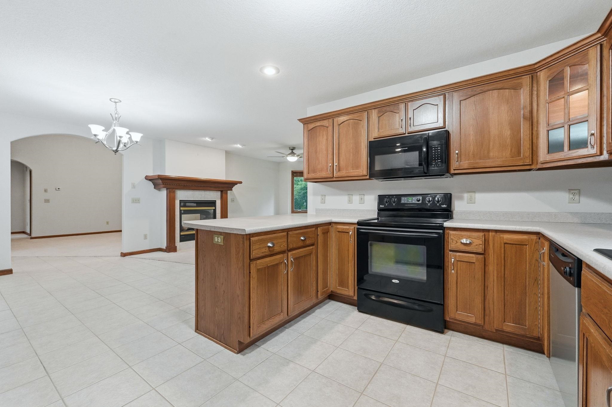 Kitchen featuring wood cabinetry, black appliances, light-toned countertops, and tile flooring