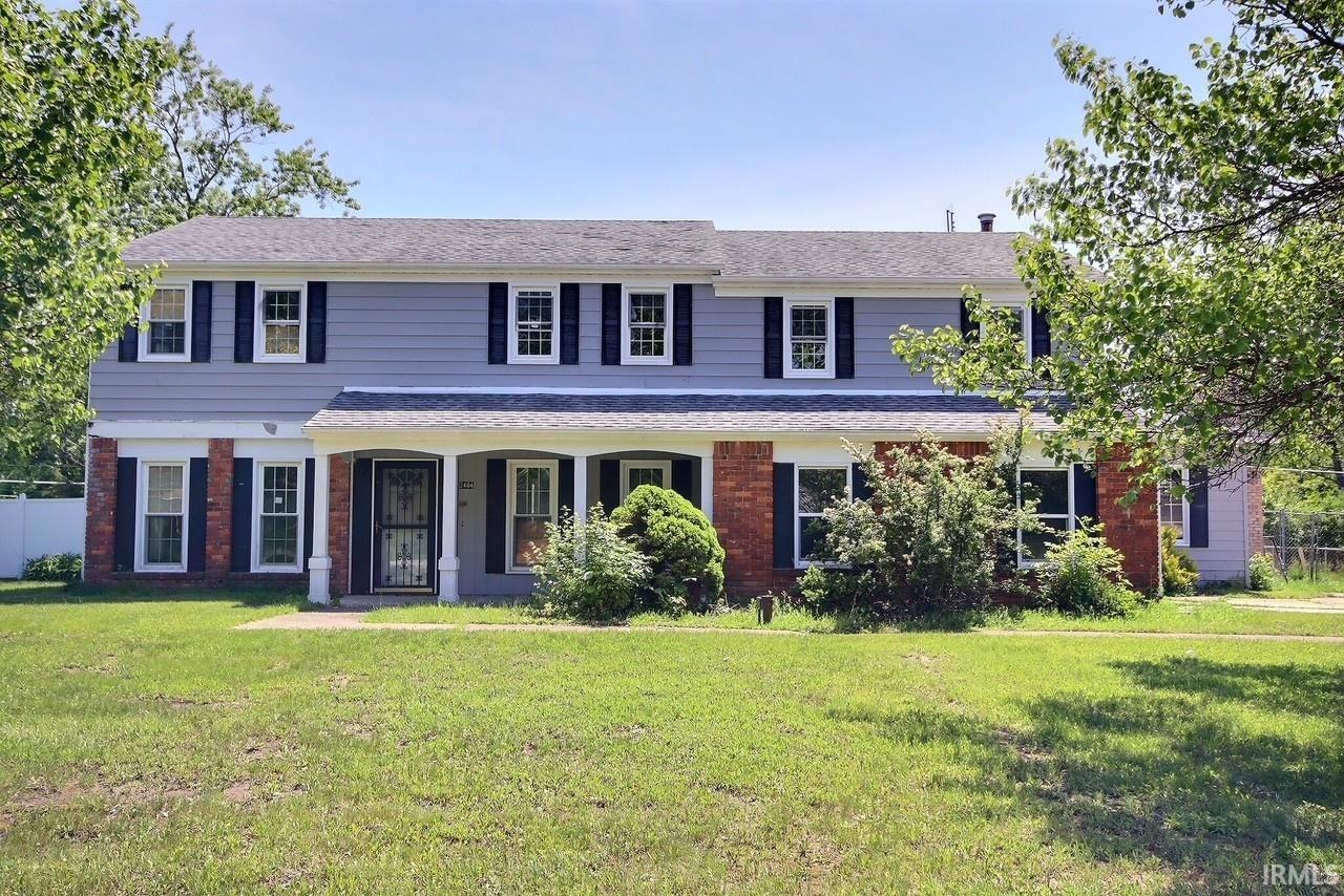 Two-story residence featuring light blue siding with brick accents, contrasting black shutters, a covered entry porch supported by white columns, and a front lawn