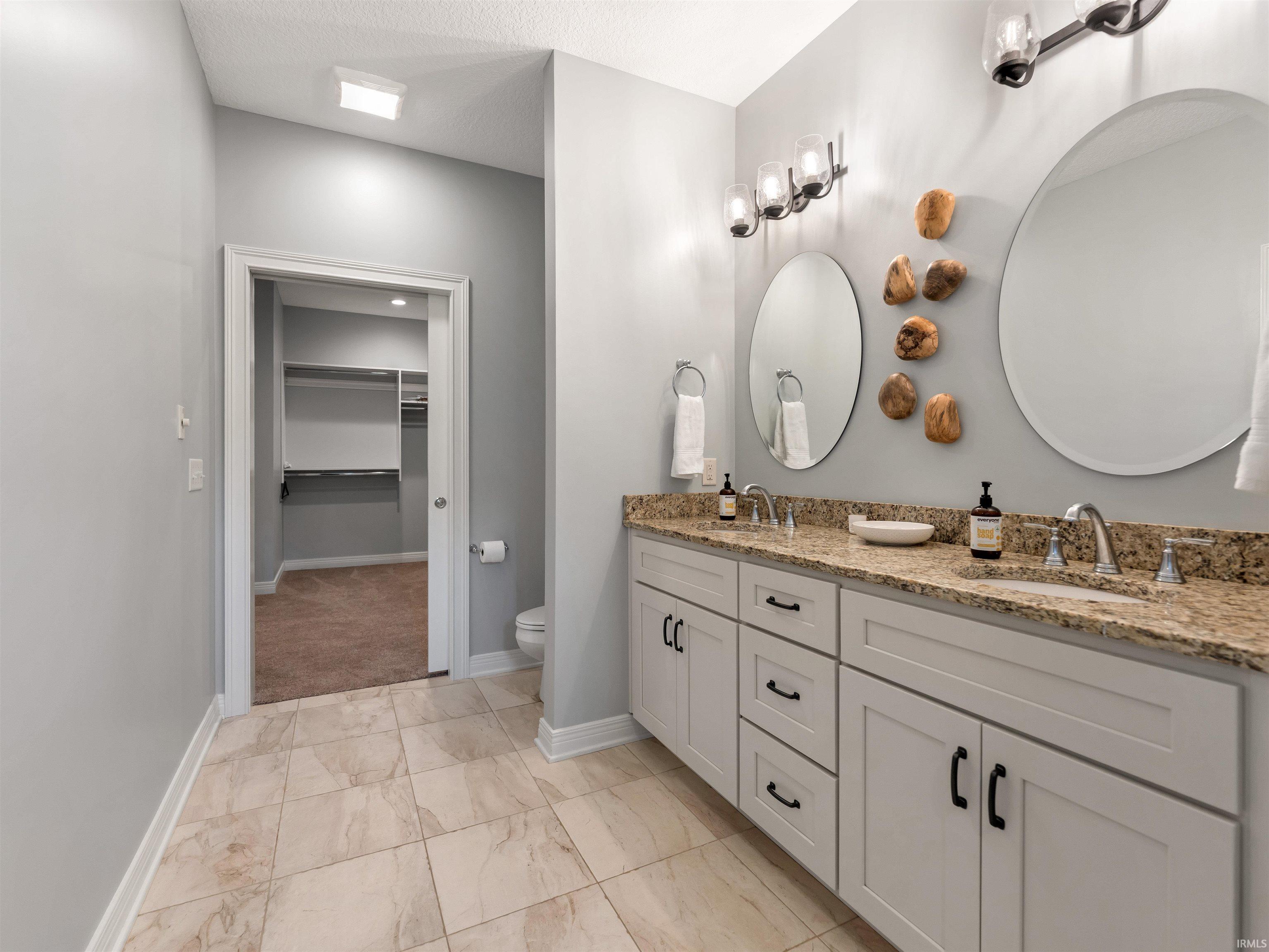 Spacious bathroom featuring a double vanity with granite countertops, light gray cabinetry, and dual round mirrors