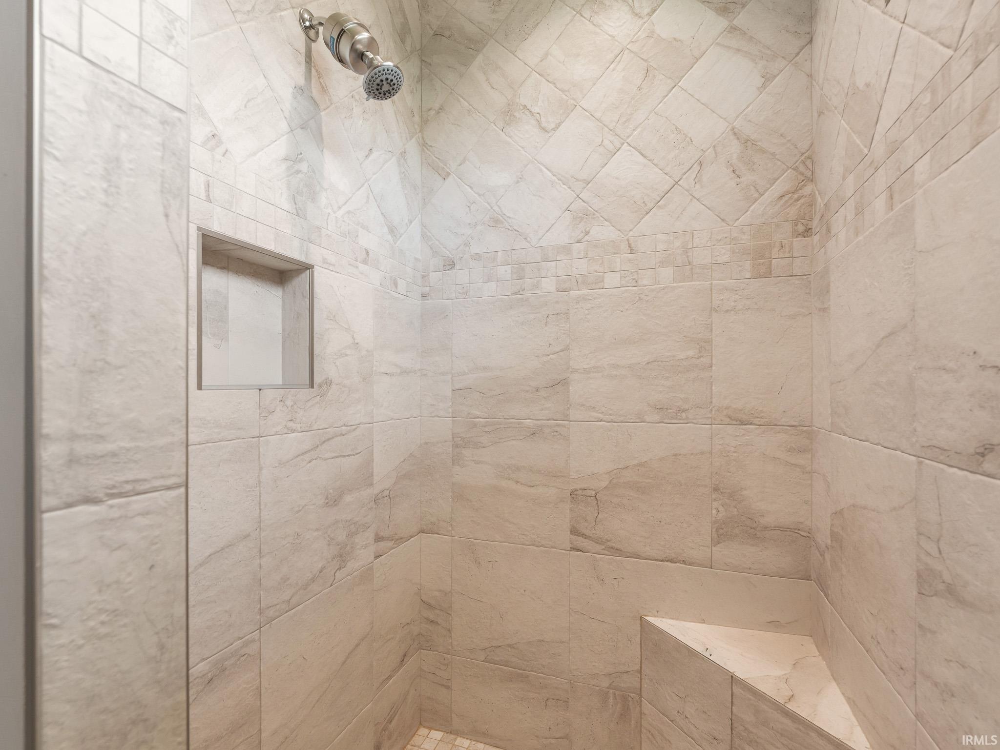 Tiled shower enclosure featuring a built-in bench, recessed niche, brushed nickel shower head, and decorative accent tile band