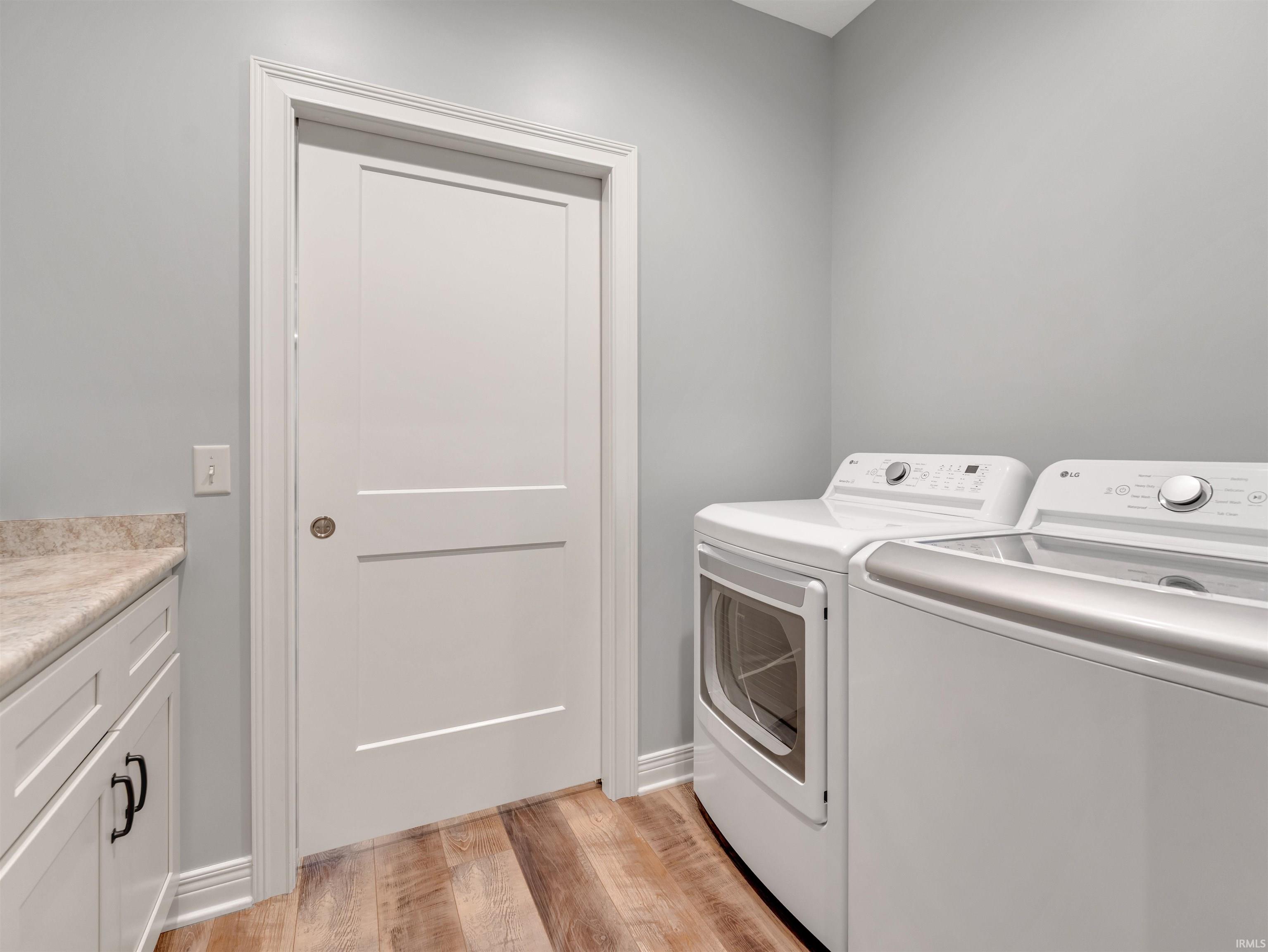 Laundry room featuring wood-finish flooring, white cabinetry with dark hardware, and a stone-look countertop