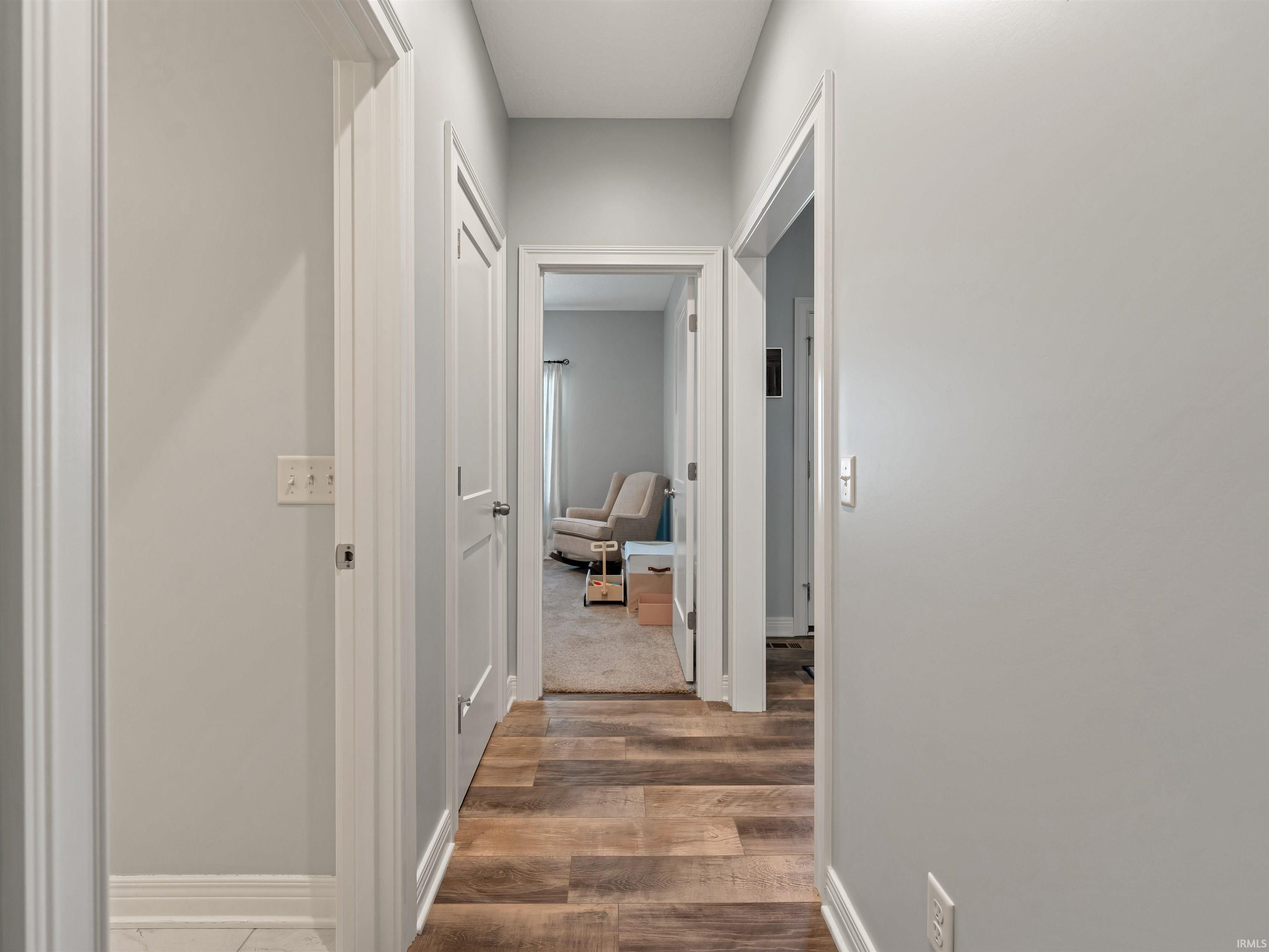 Hallway with wood-finish flooring, light gray wall paint, white trim, and multiple doorways