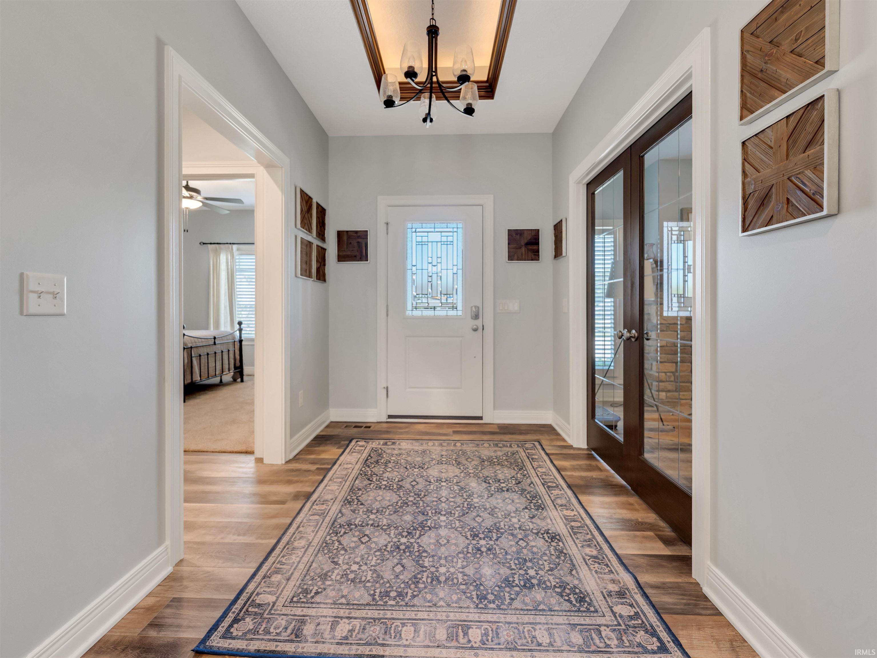 Entryway featuring wood-finish flooring, a decorative inlaid ceiling with an attached chandelier, and a white front door with decorative glass inserts