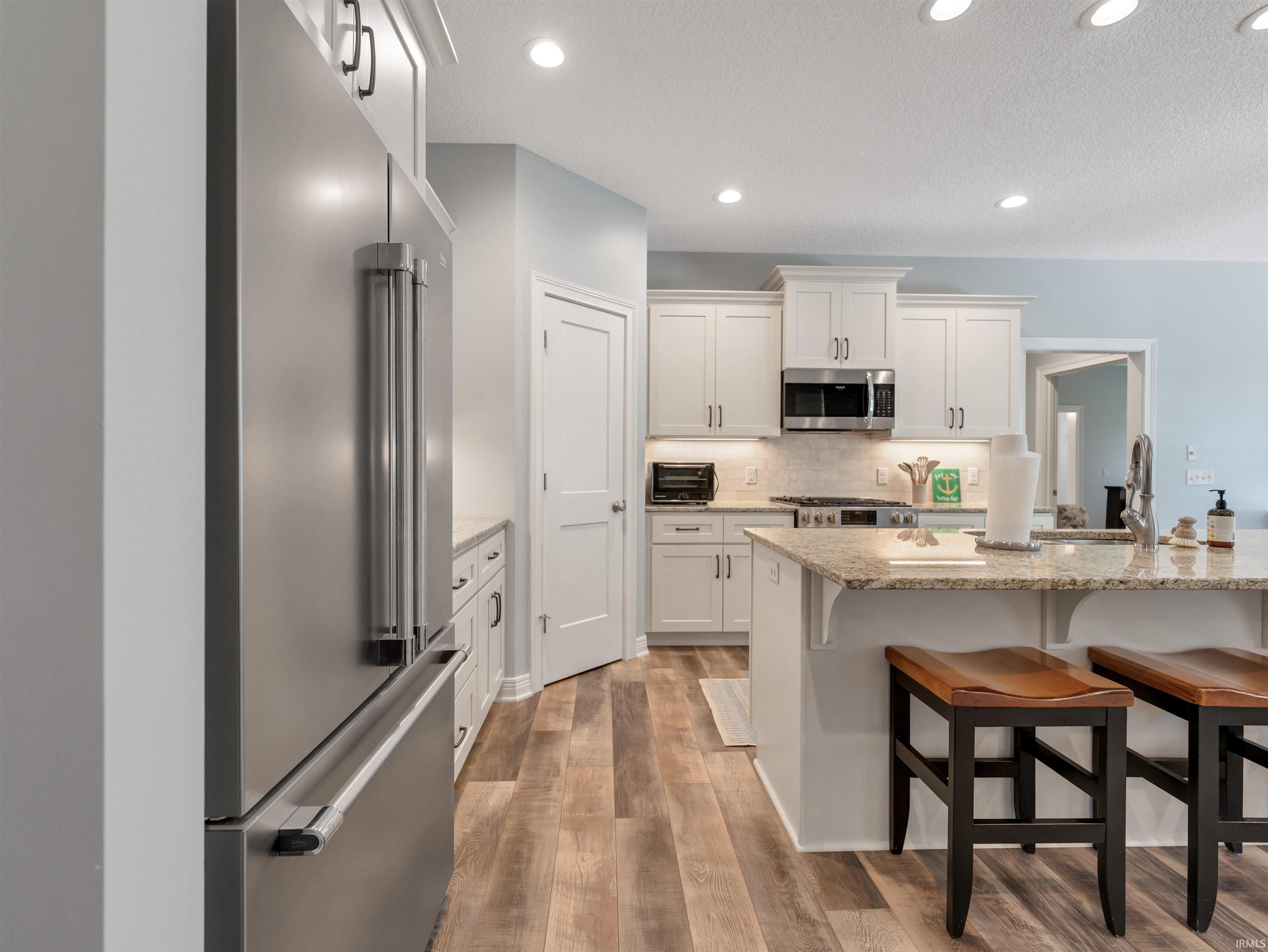 Kitchen featuring stainless steel appliances, white cabinetry with dark hardware, a light-colored tile backsplash, a kitchen island with stone countertops, and wood-finish flooring