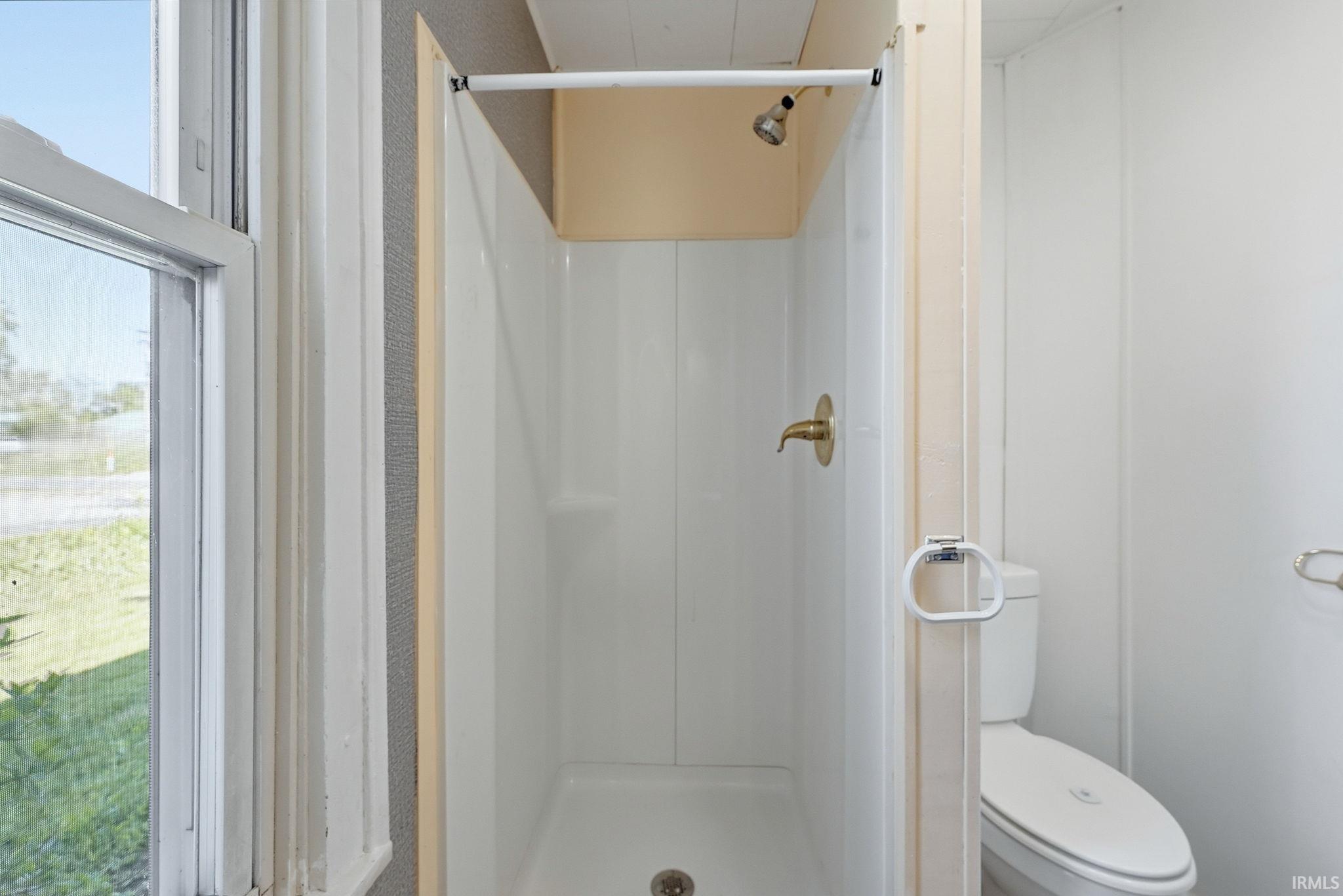 Shower stall featuring a white surround, brass-finish fixtures, and a shower curtain rod