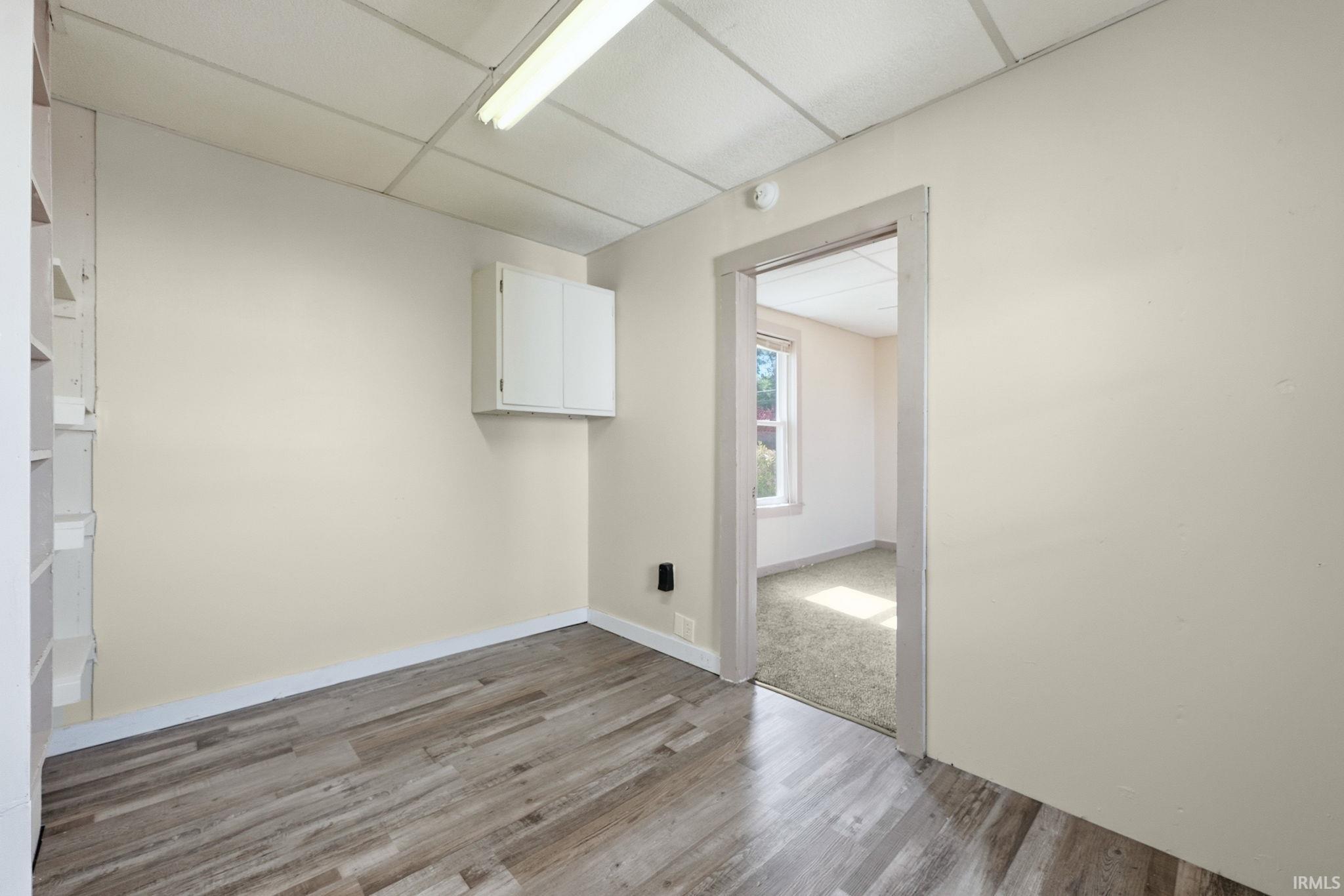 Interior room featuring wood-finish flooring, white baseboards, a white wall-mounted cabinet, and a built-in shelving unit