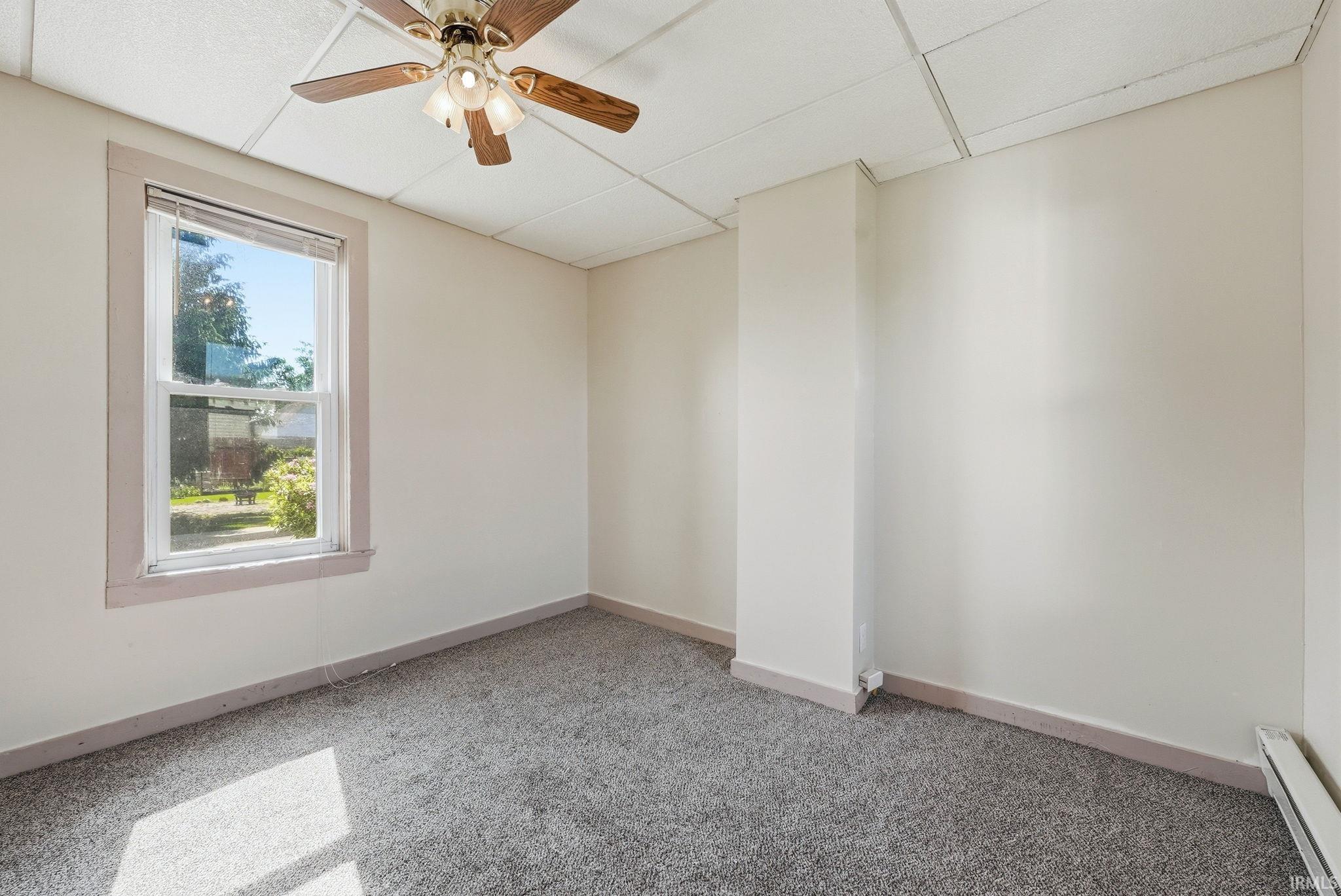 Room featuring a ceiling fan with integrated lighting, a single pane window, neutral wall paint, and grey carpet flooring