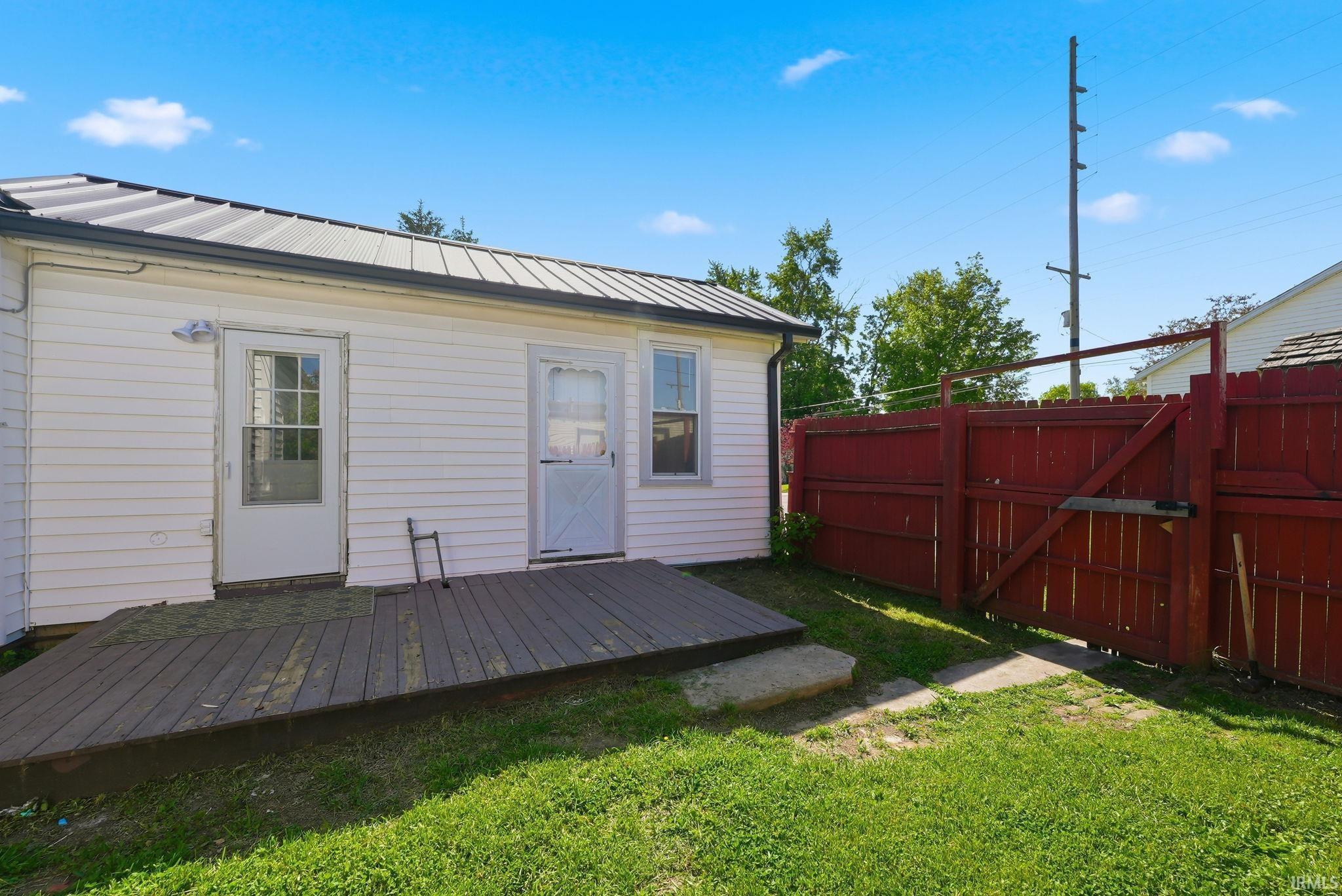 Backyard featuring a wooden deck, white siding, and a red privacy fence