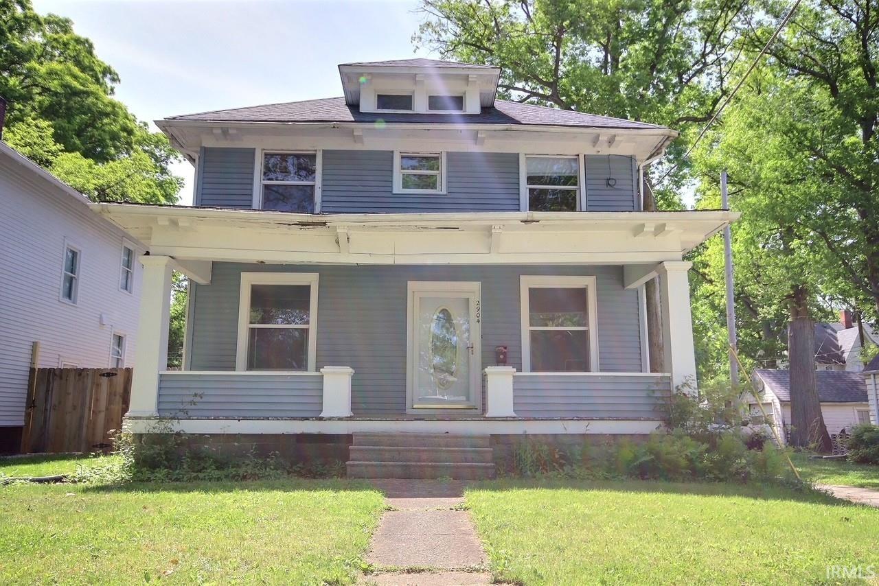 Two-story residence featuring light blue siding with white trim, a covered front porch, and a front yard with a concrete pathway