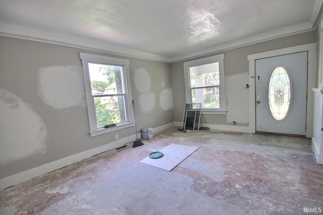 Entryway featuring a decorative oval glass door, two windows with white trim, crown molding, and baseboards
