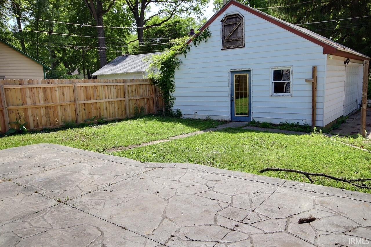 Backyard featuring a stamped concrete patio, a private wood fence, and a detached structure with siding and an upper-level dormer