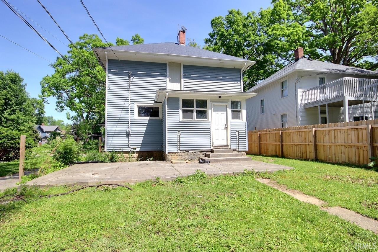 Rear exterior featuring light blue horizontal siding, a white entry door, and a concrete patio
