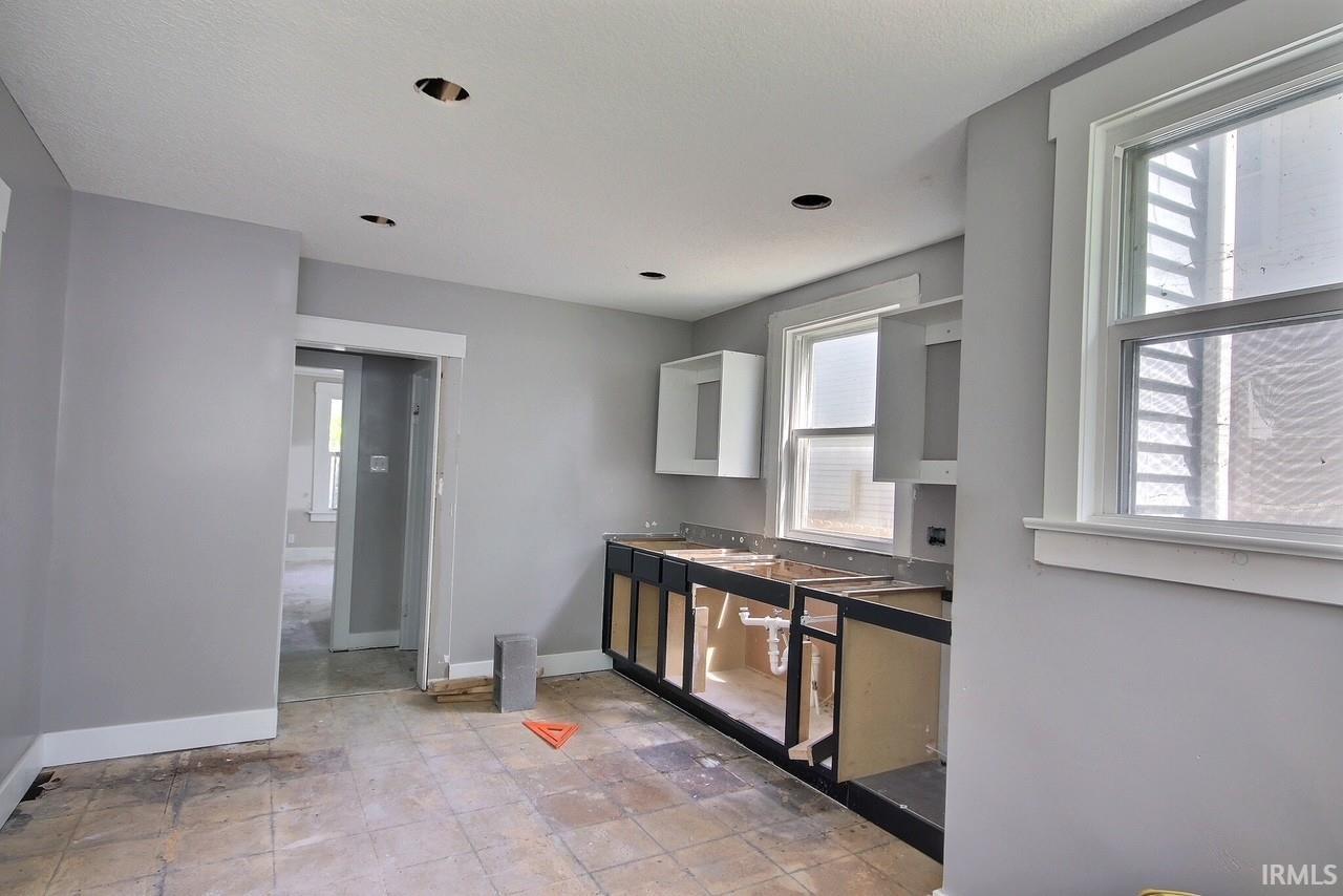 Kitchen space featuring upper and lower cabinetry, two windows with white trim, recessed ceiling lighting, and a doorway