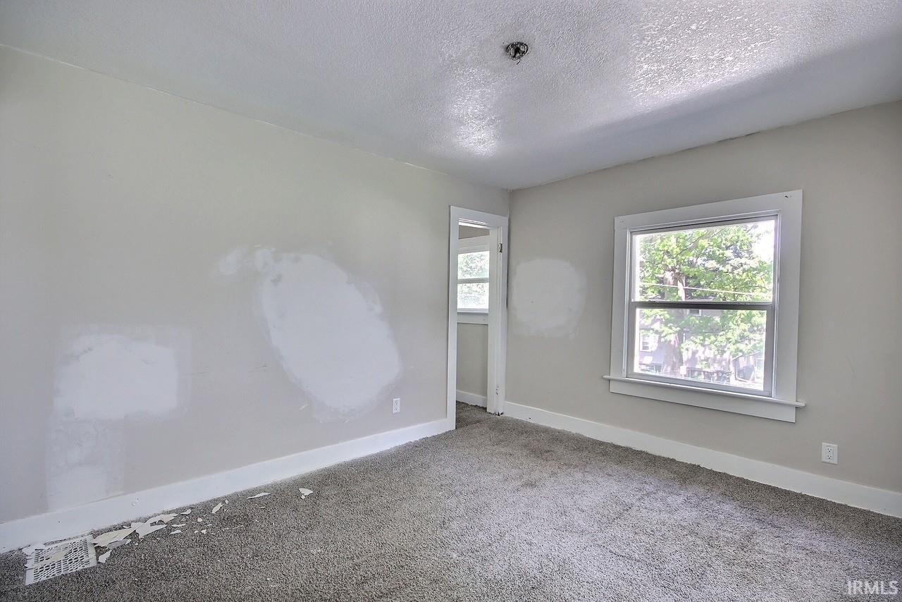 Carpeted room featuring a single window with white trim, light gray walls, and a recessed doorway