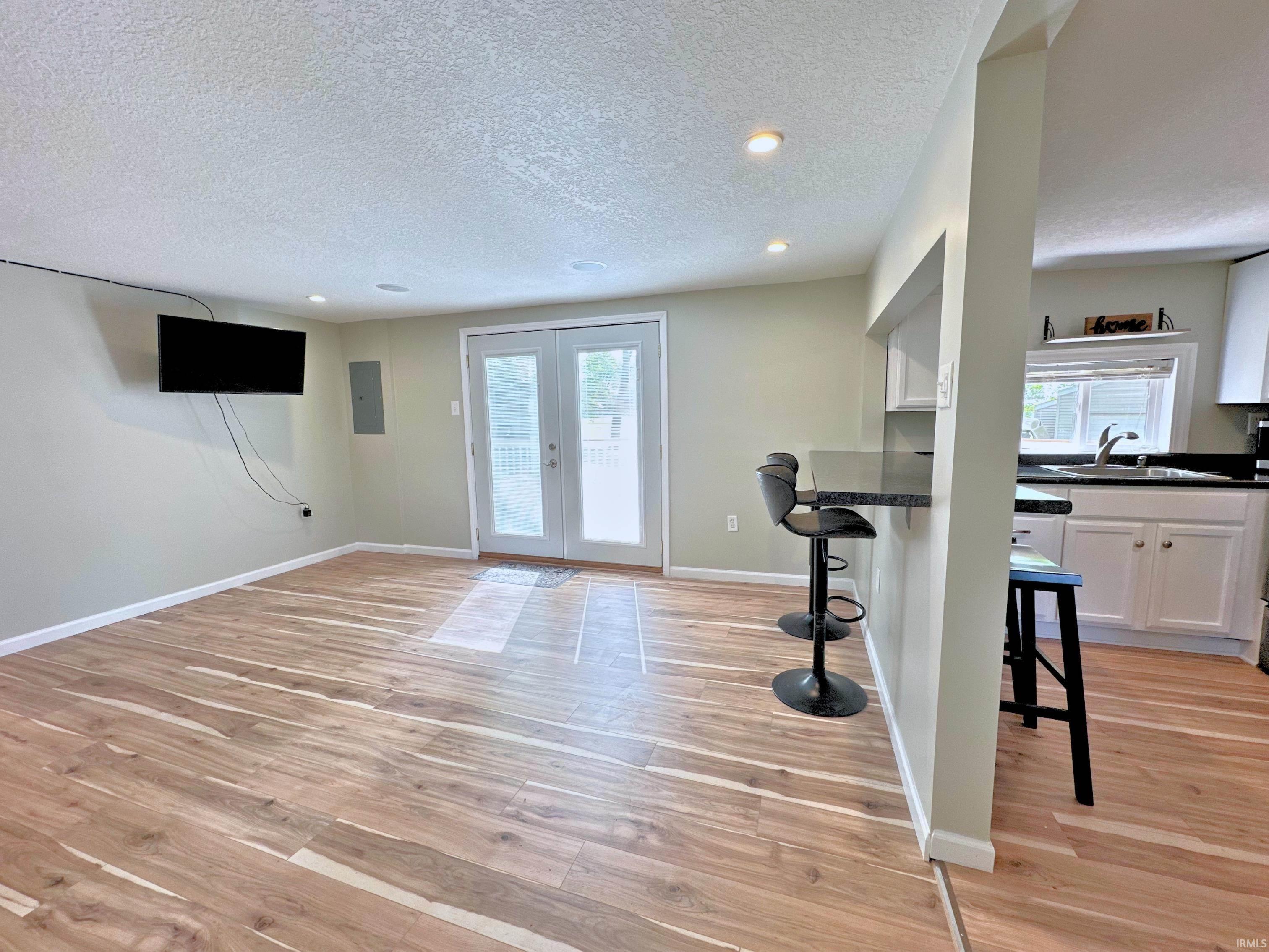 Open-concept living area with wood flooring, recessed lighting, in-house surround sound, and direct patio access through double French doors. Entertain guests through the breakfast counter and pass-through.