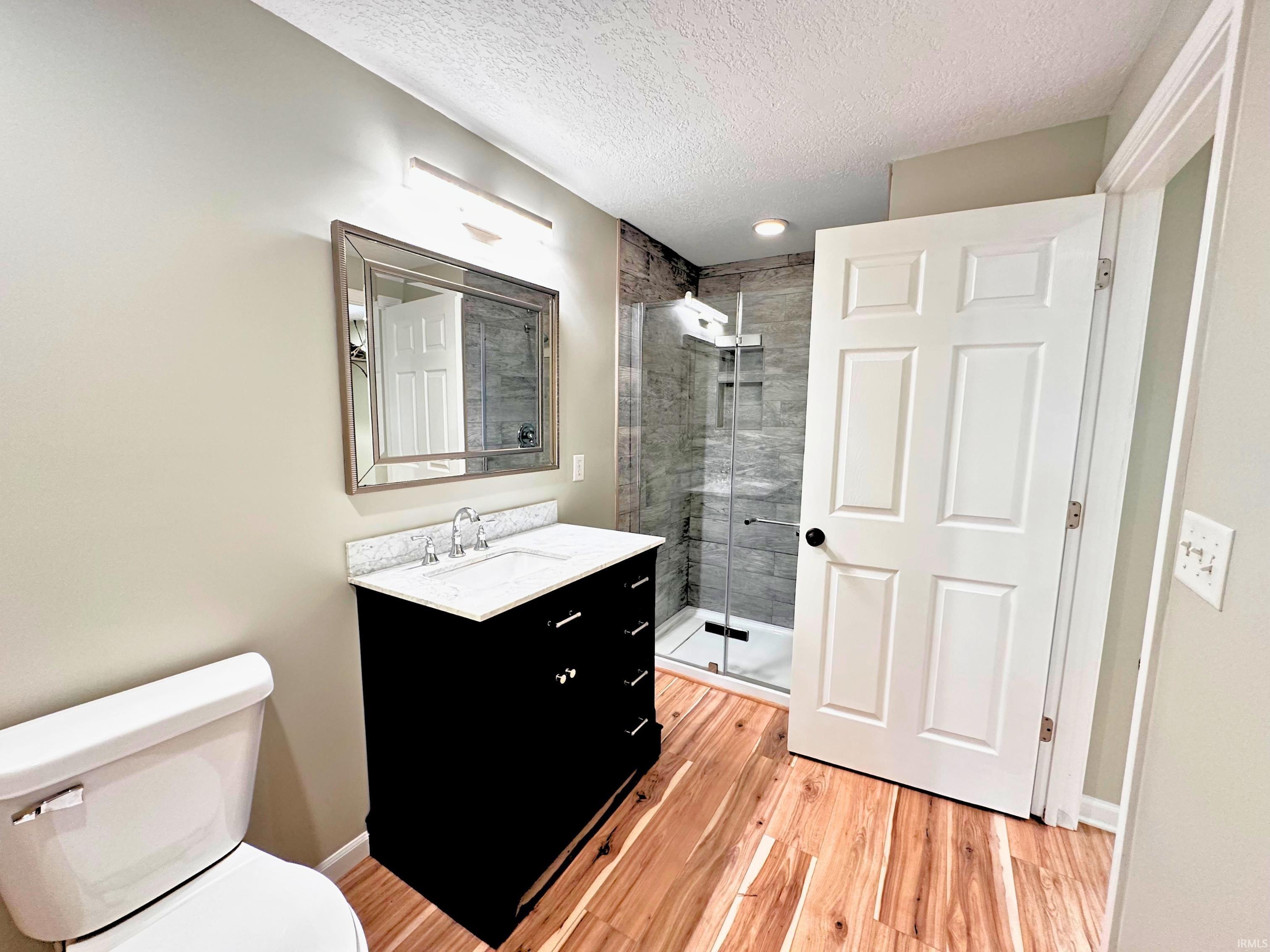 Contemporary bathroom featuring a black vanity with a light-toned countertop, a frameless shower enclosure with gray tile, and warm wood-finish flooring