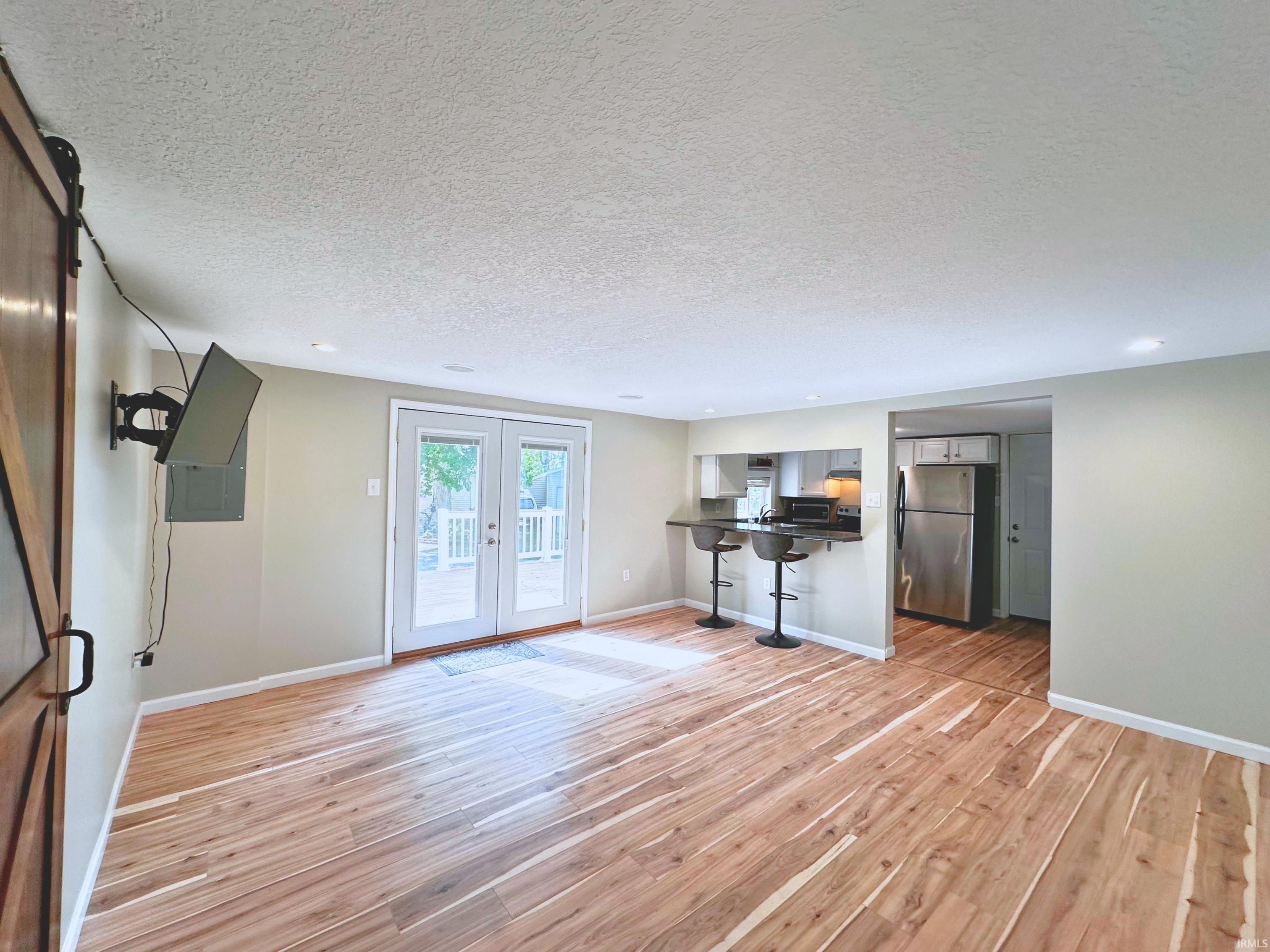 Spacious living area featuring wood-finish flooring, recessed lighting, and light-toned walls. French-doors leading to the open poly-wood deck.