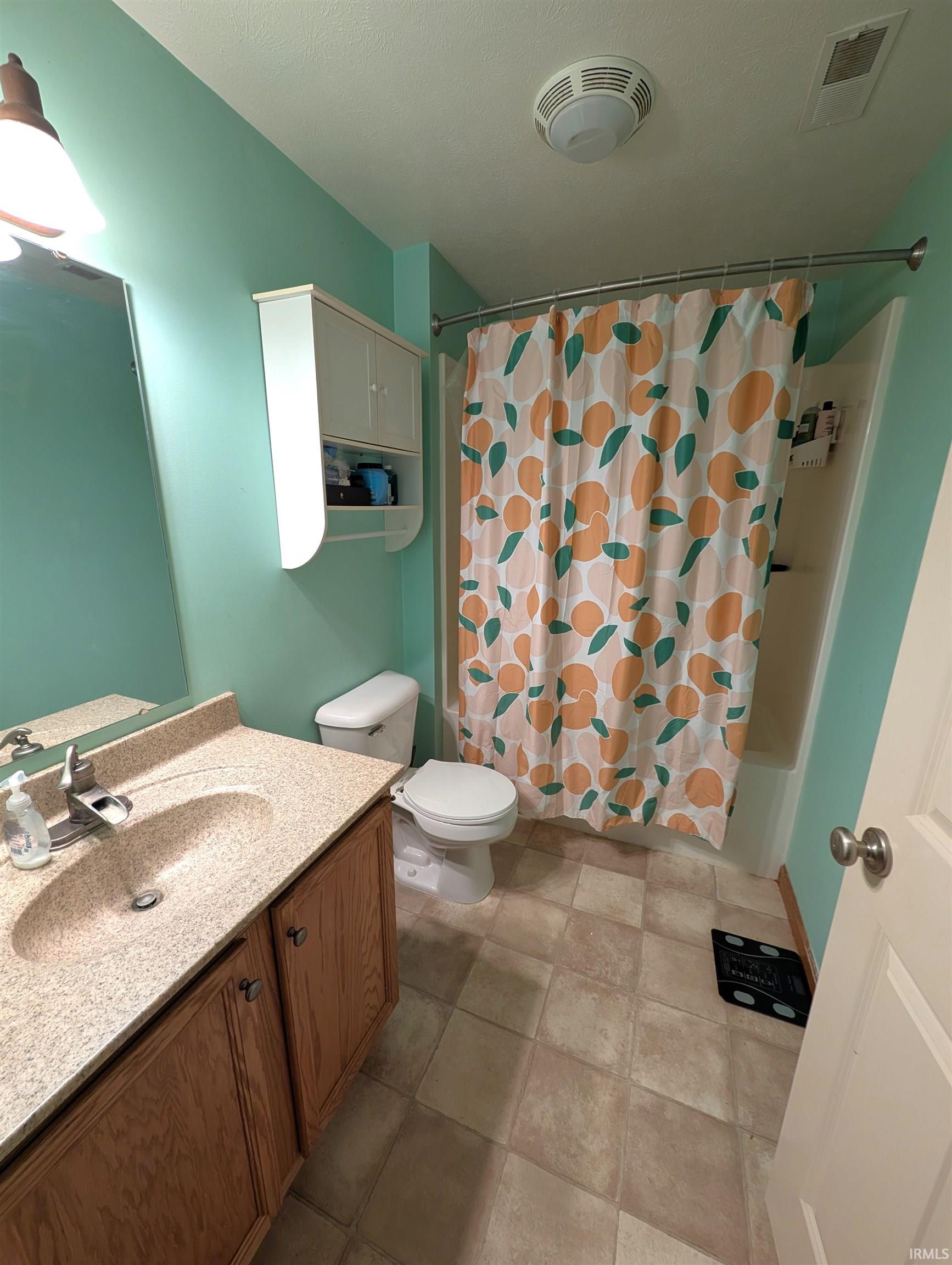 Bathroom featuring a light wood vanity with a speckled countertop and integrated sink, a commode, and a shower with a curved curtain rod