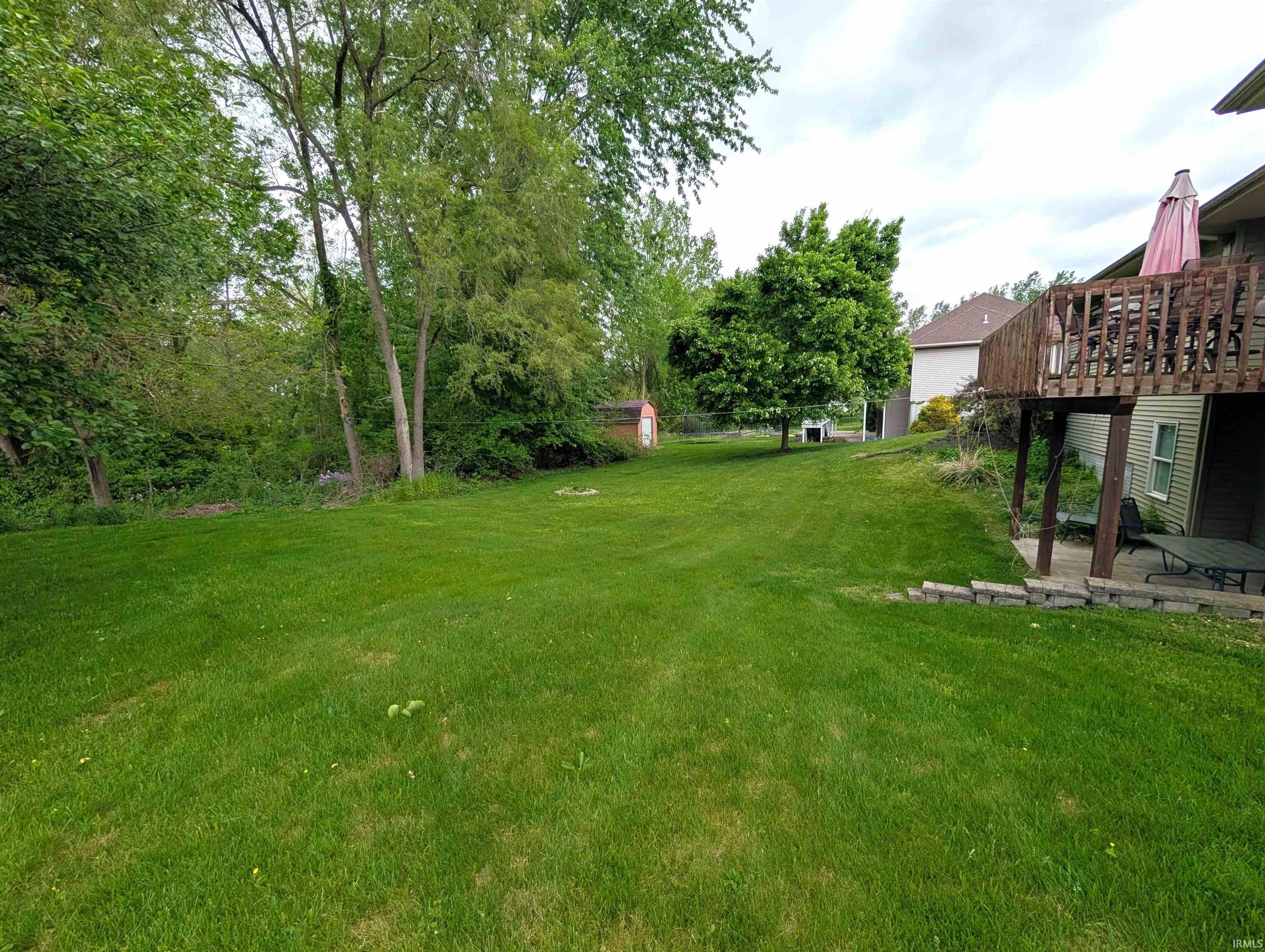 Expansive rear yard featuring a large green lawn, mature trees, a multi-level wooden deck, and a lower patio area
