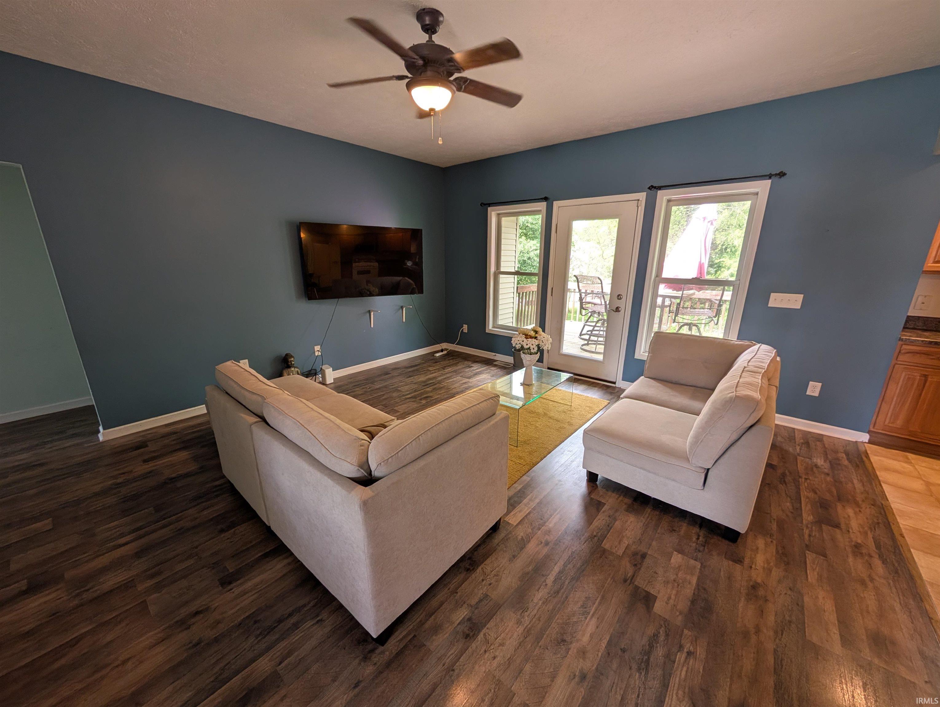 Living area featuring wood-finish flooring, a ceiling fan with integrated lighting, and direct access to an outdoor deck through a glass-paneled door