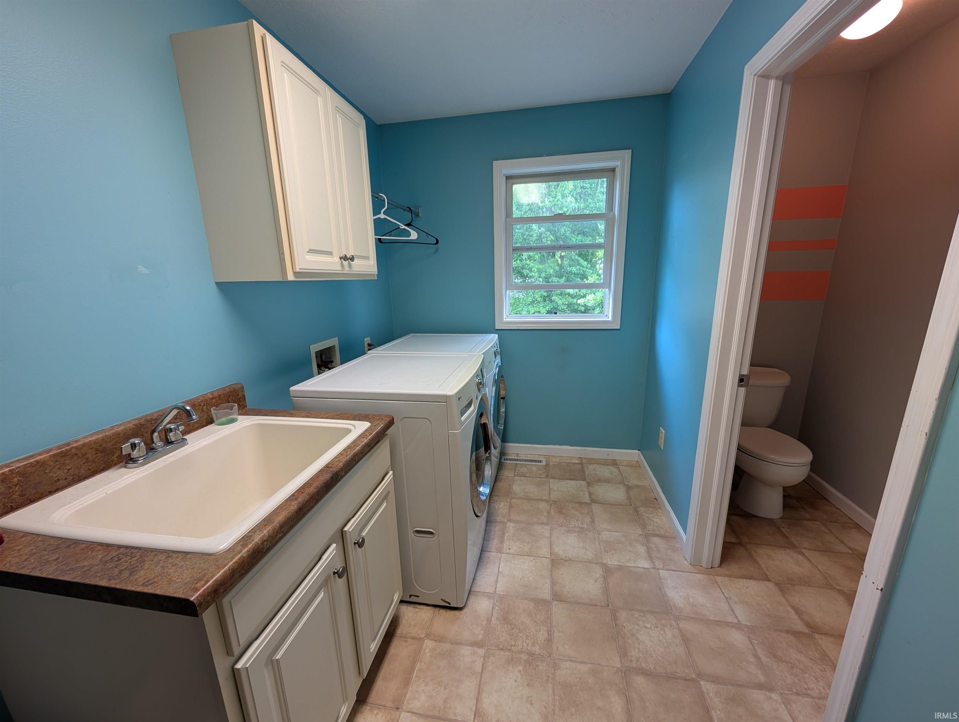 Functional laundry room featuring a utility sink with a laminate countertop, white cabinetry, and durable tile flooring