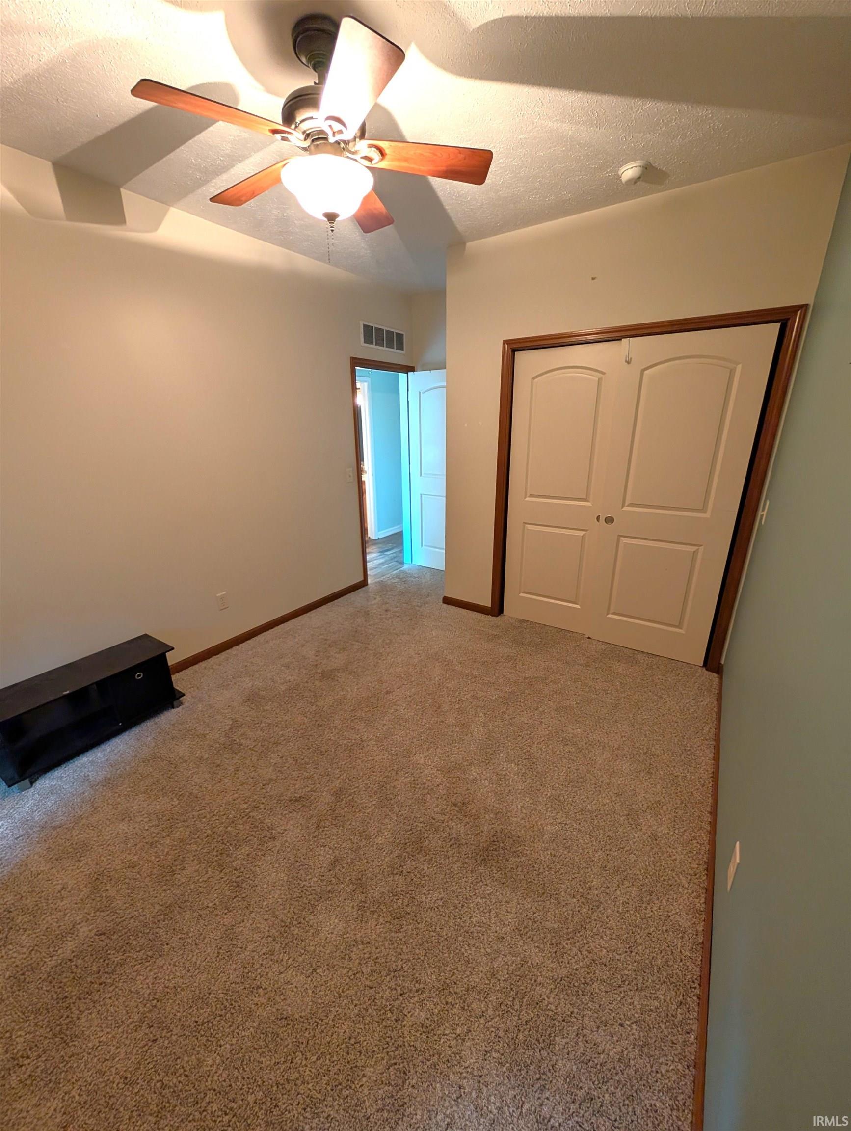 Carpeted room featuring a ceiling fan with integrated lighting, tray ceiling detail, bi-fold closet doors, and wood-finish baseboards