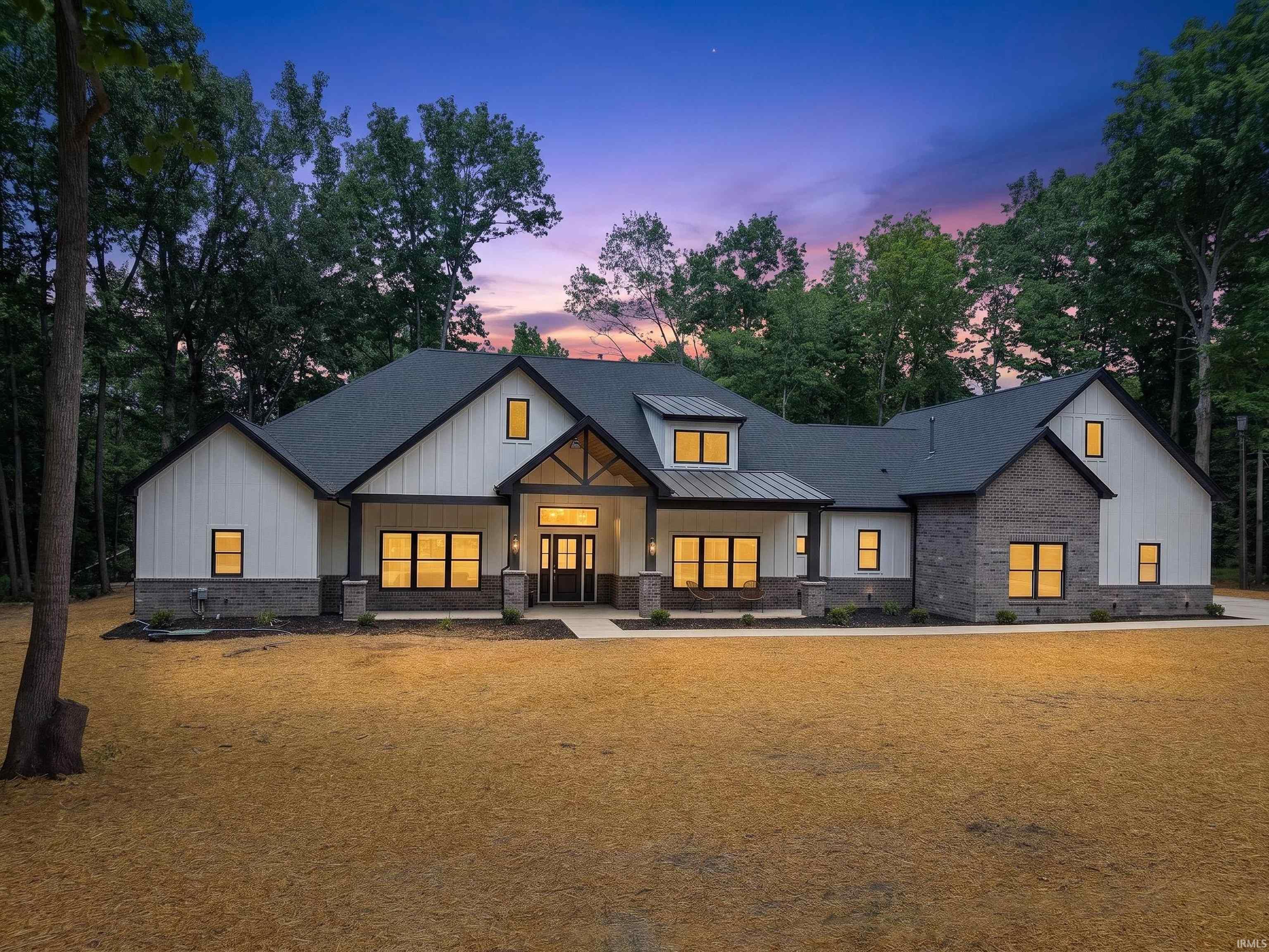Modern farmhouse exterior featuring board and batten siding, dark brick accents, a dark shingle roof, and a prominent covered entry with exposed wood beams