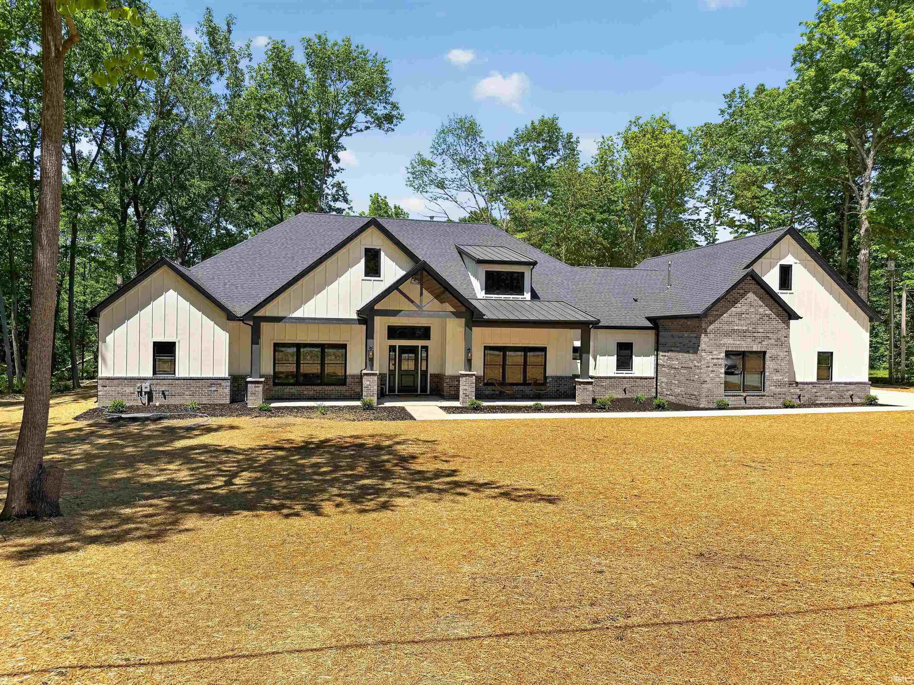Modern farmhouse exterior featuring board and batten siding, stone accents, dark-framed windows, a covered entry with exposed trusses, and a dark shingle roof