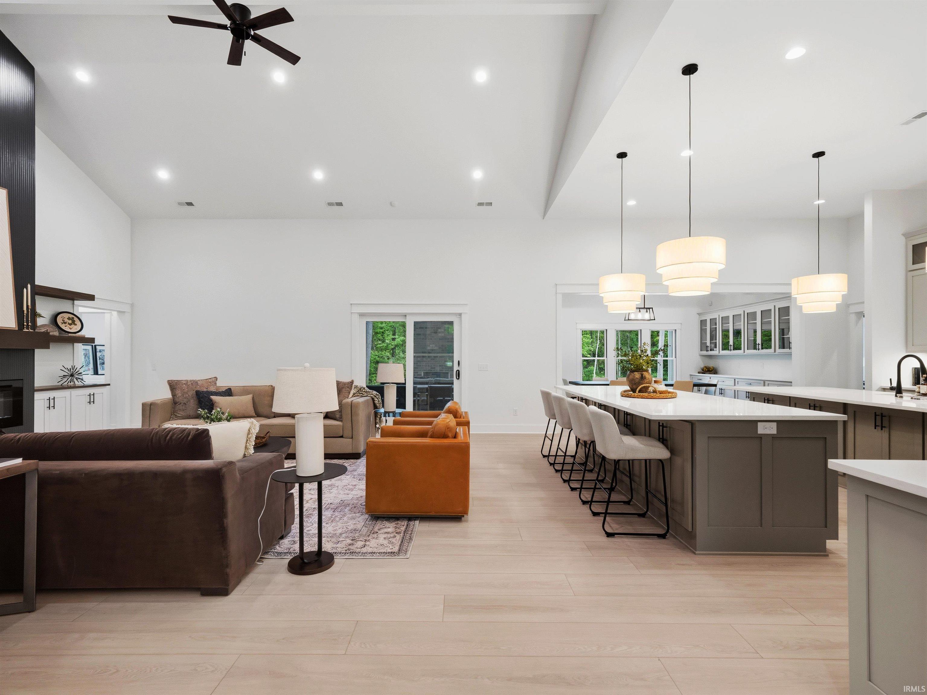 Open-concept living space featuring light wood-finish flooring, a vaulted ceiling with recessed lighting and a ceiling fan, and a built-in fireplace with a dark surround