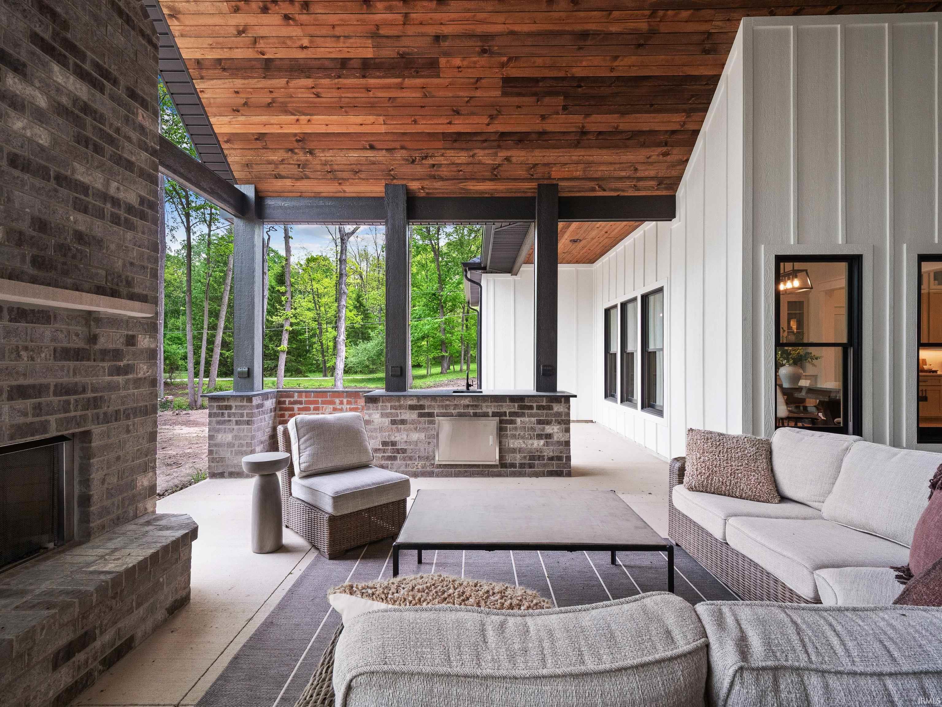 Covered outdoor living space featuring a brick fireplace with a floating mantel, a wood-plank ceiling, and board-and-batten siding