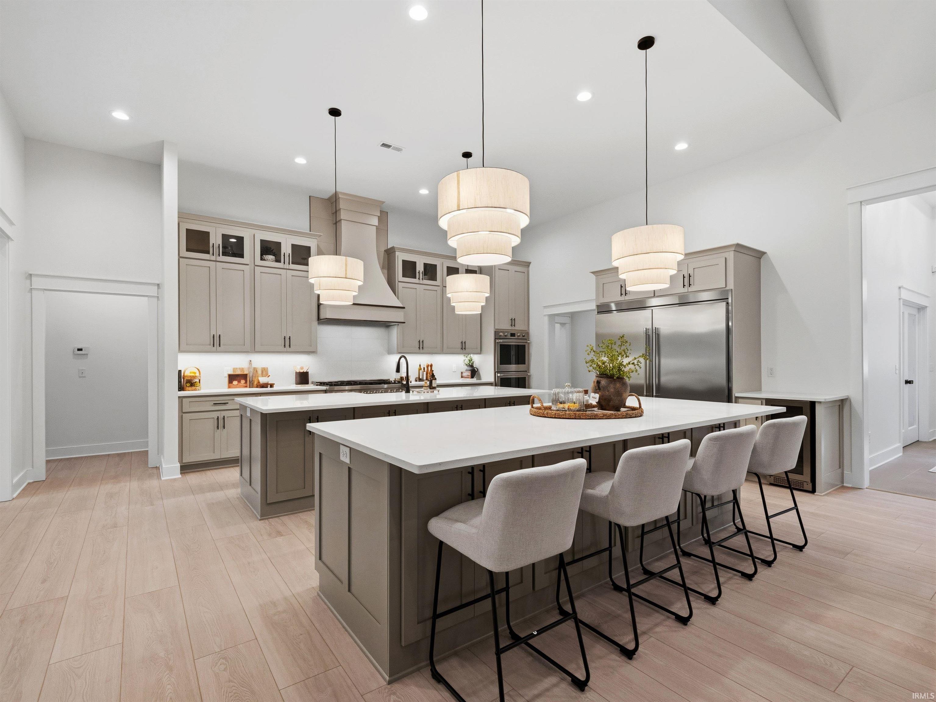 Spacious kitchen featuring two islands with white countertops, light wood-finish flooring, and recessed lighting