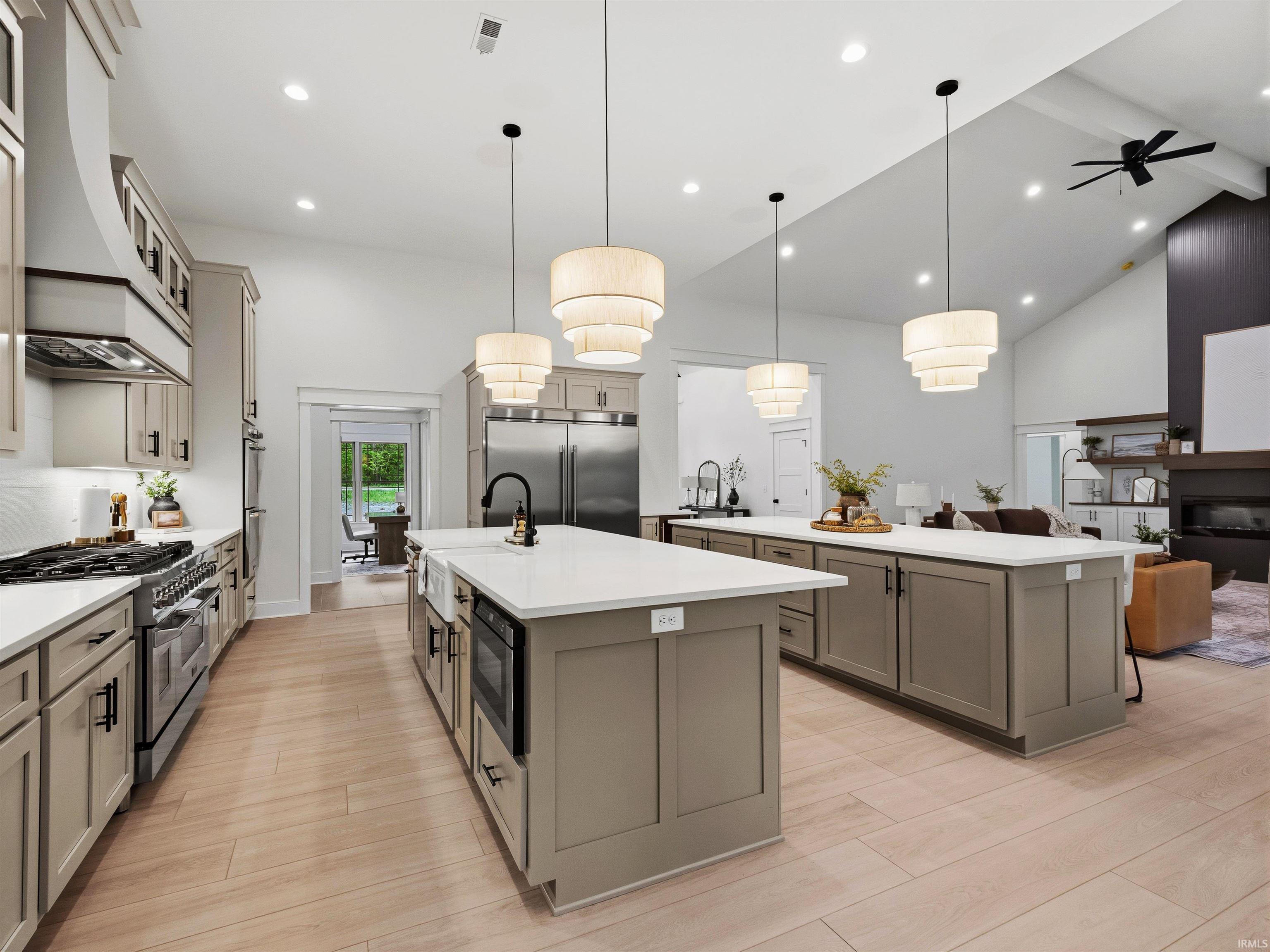 Open-concept kitchen featuring two islands with white countertops, light wood-finish flooring, and a vaulted ceiling