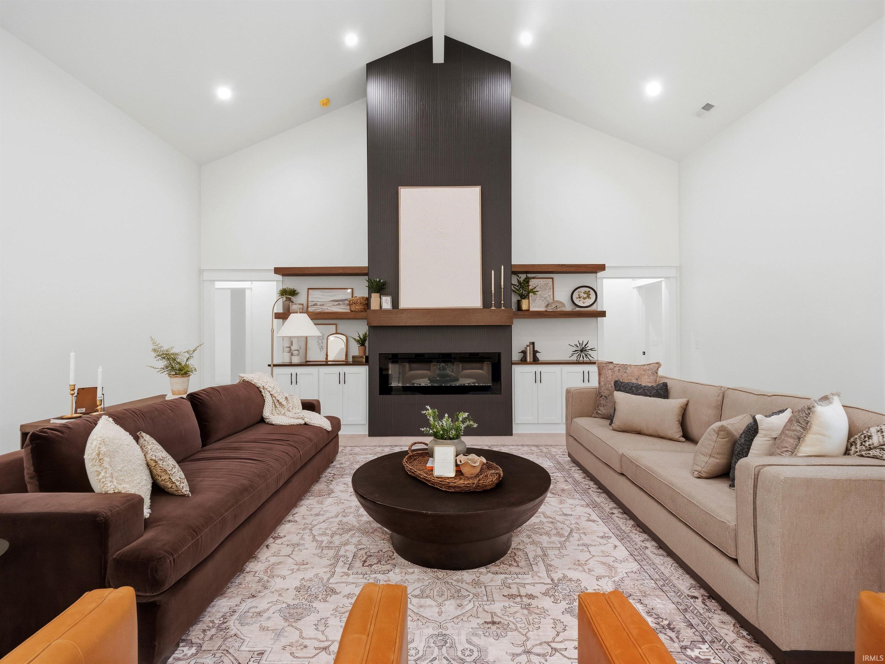 Vaulted ceiling living space featuring a modern fireplace with a dark surround, a substantial wood mantel, and built-in white cabinetry with floating wood shelves
