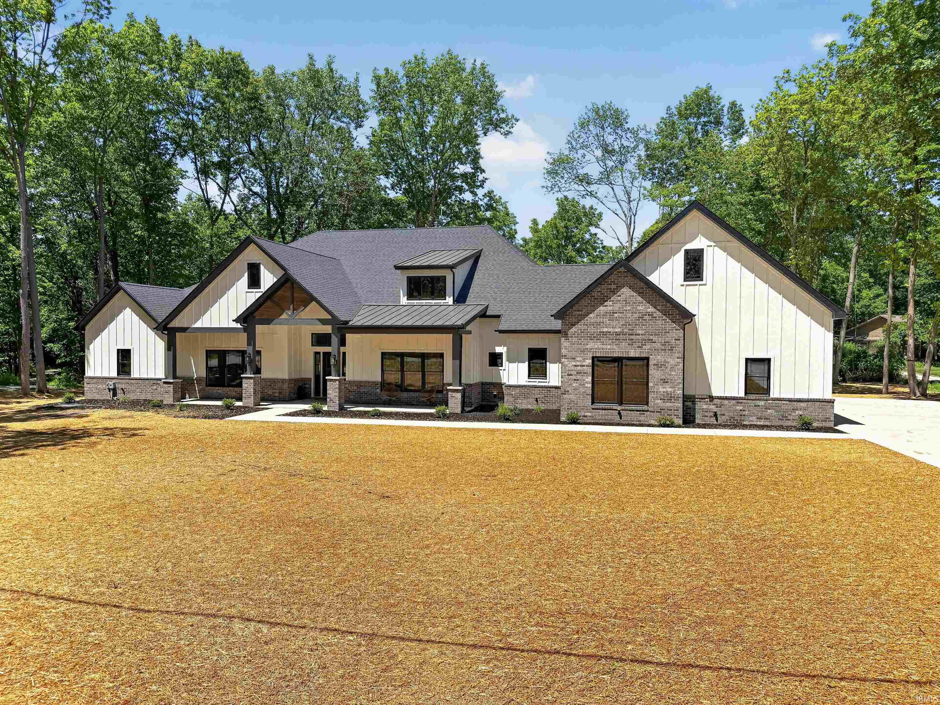 Contemporary residence featuring a blend of white board-and-batten siding and dark brick, a dark shingled roof, a covered front entry, and multiple dark-framed windows