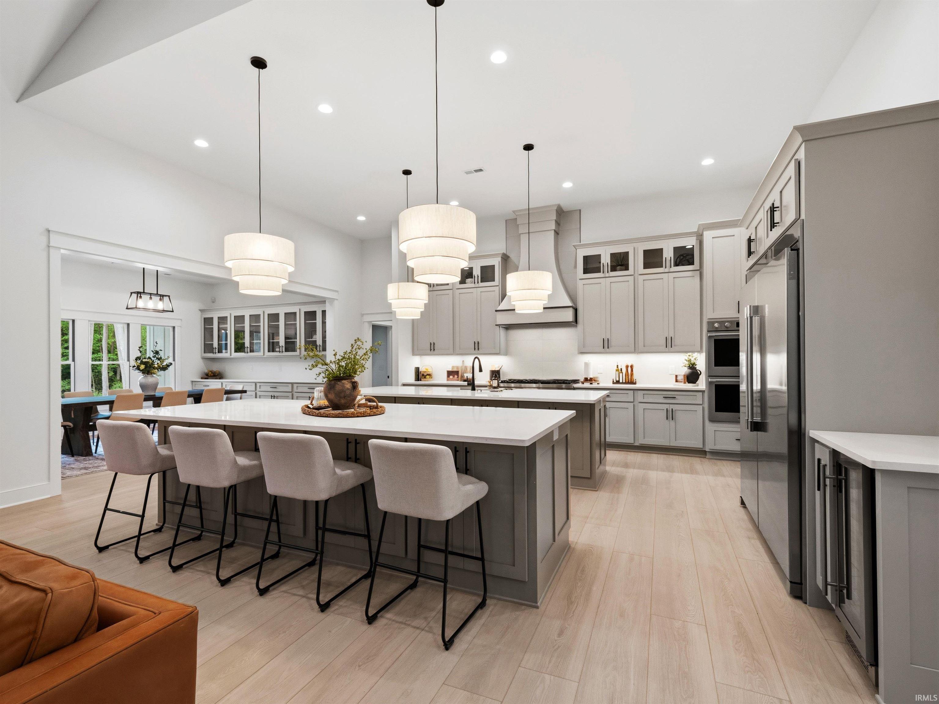 Open concept kitchen featuring two islands with white countertops, light wood-finish flooring, and light gray cabinetry