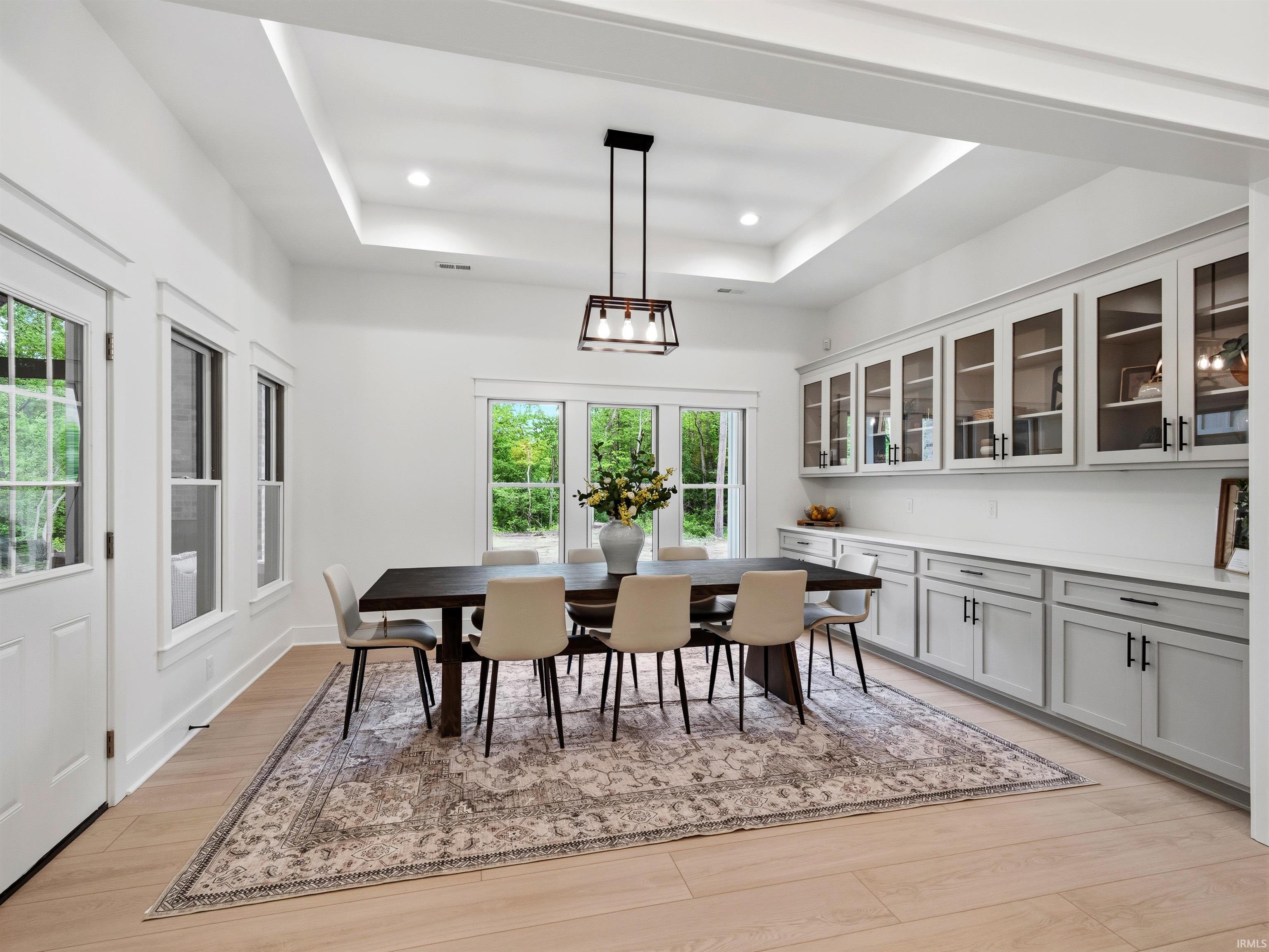 Bright dining area featuring light wood-finish flooring, a tray ceiling with recessed lighting, and a linear chandelier
