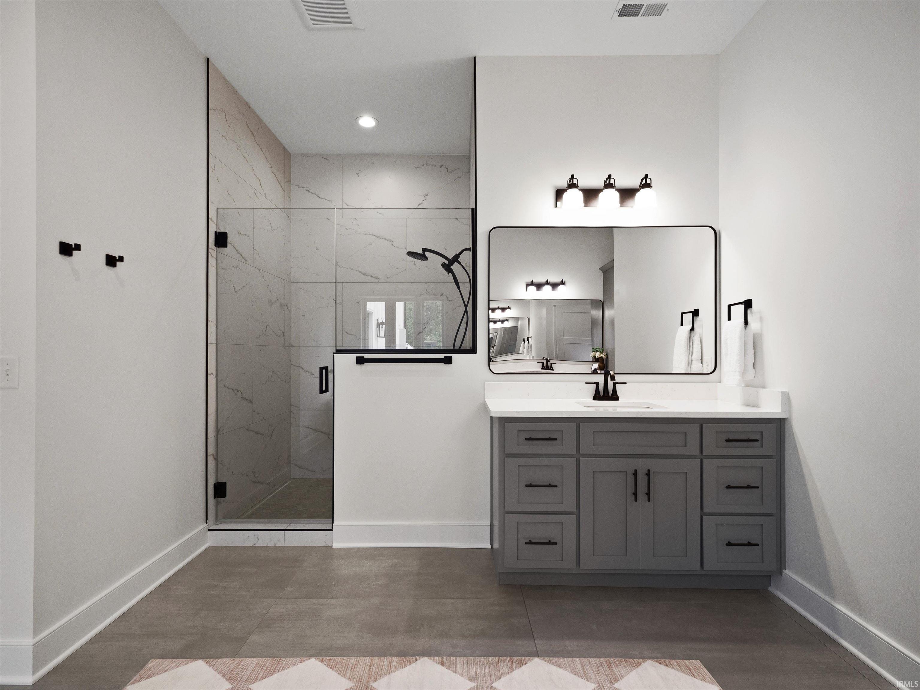 Contemporary bathroom featuring a spacious walk-in shower with clear glass enclosure and light-toned tile walls, a vanity with a white countertop and gray cabinetry, a rectangular mirror with a black frame, and matte black hardware throughout