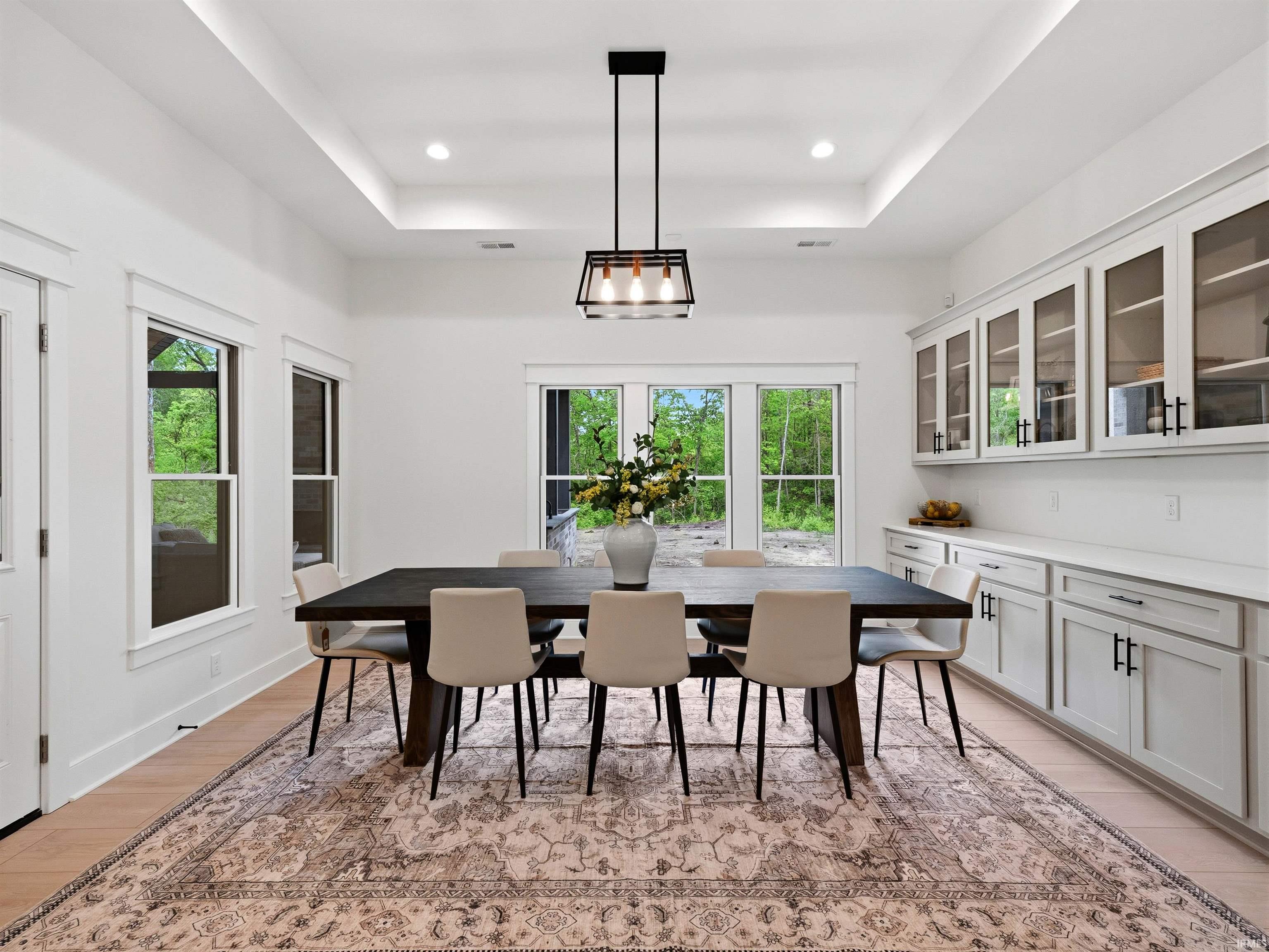 Modern dining room featuring light wood-finish flooring and a tray ceiling with recessed lighting