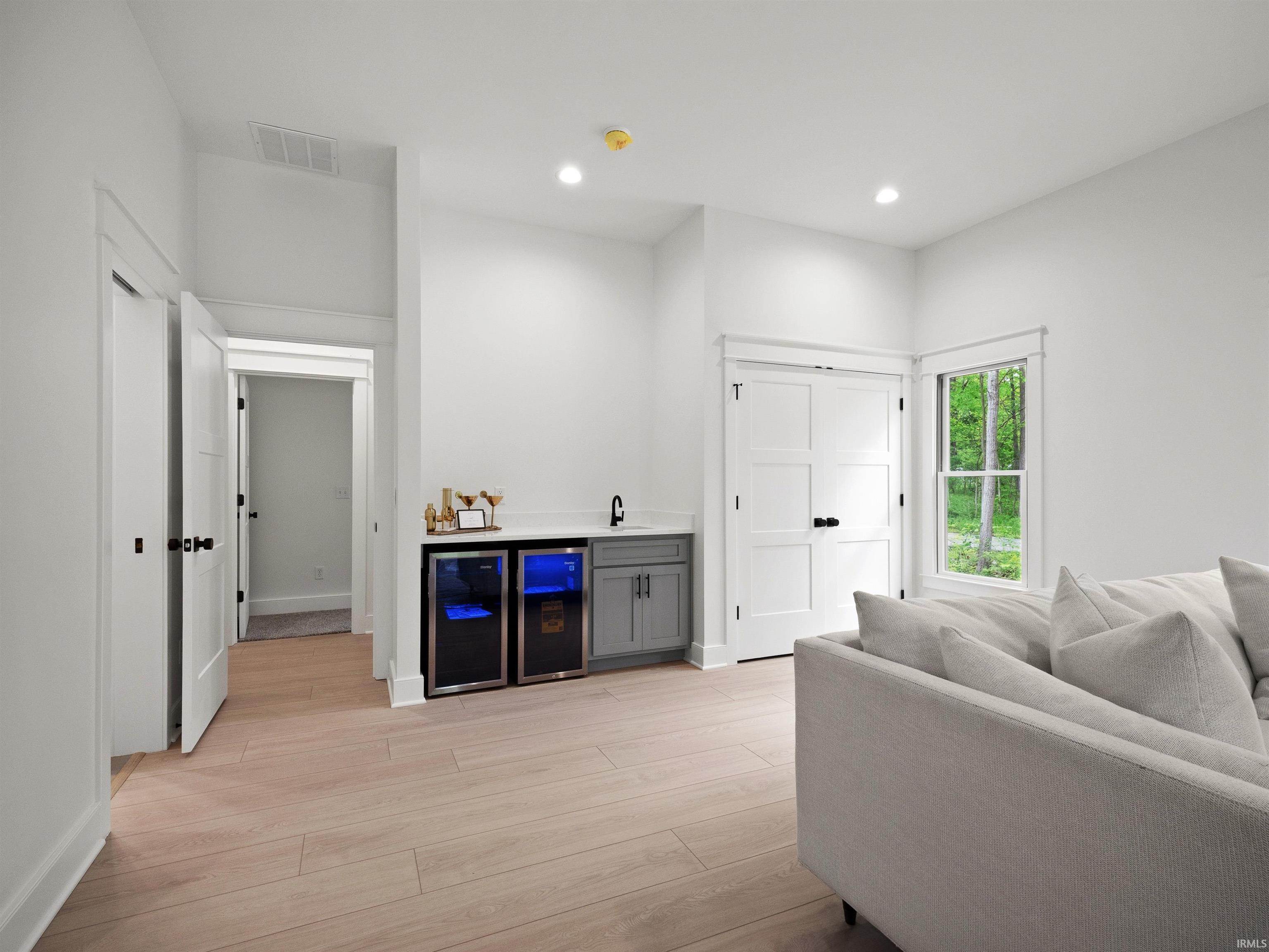 Entertainment area featuring wood-finish flooring, recessed lighting, and a wet bar with dual beverage refrigerators