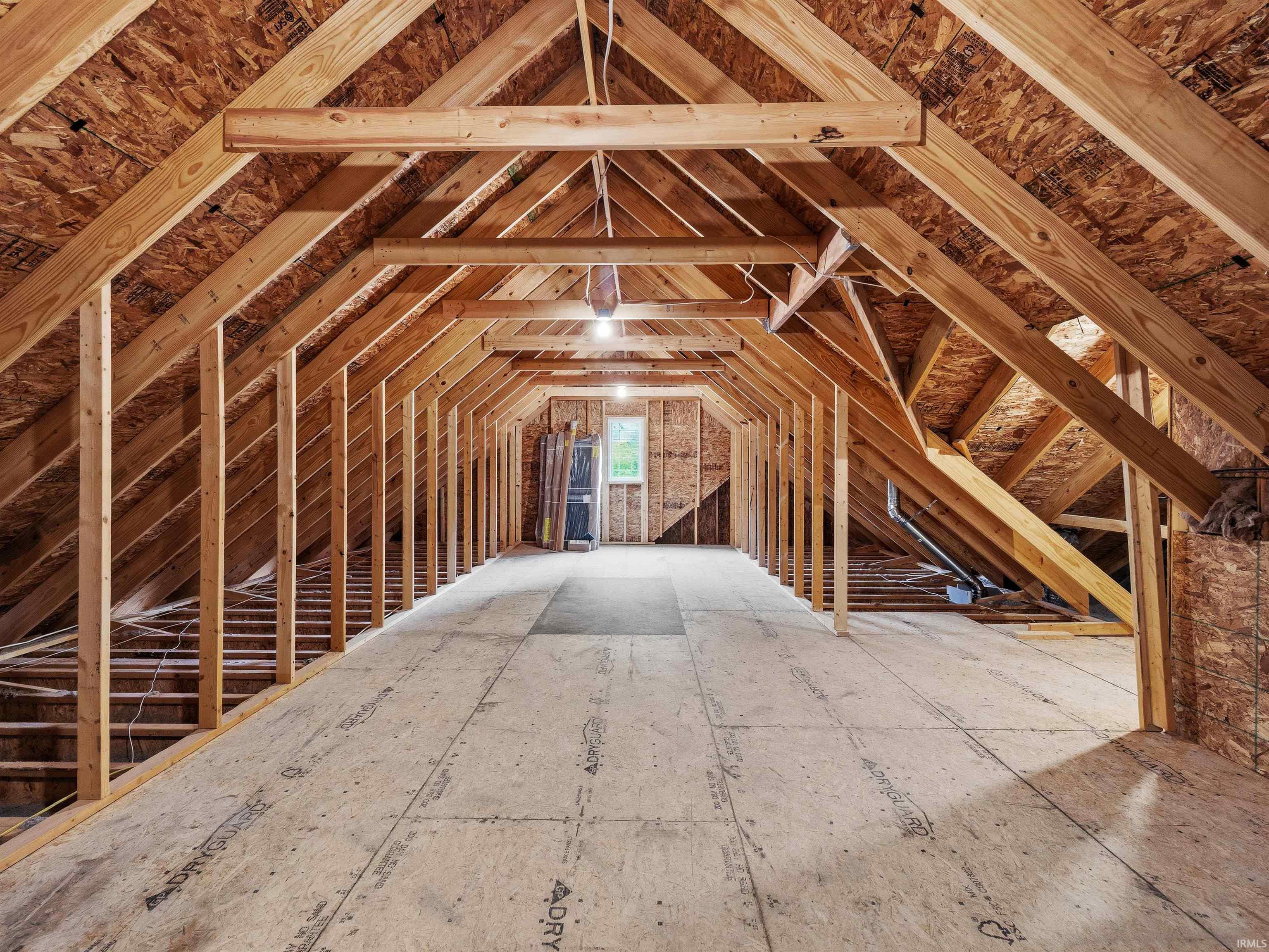 Expansive unfinished attic space featuring exposed wood framing, plywood flooring, and a rear window