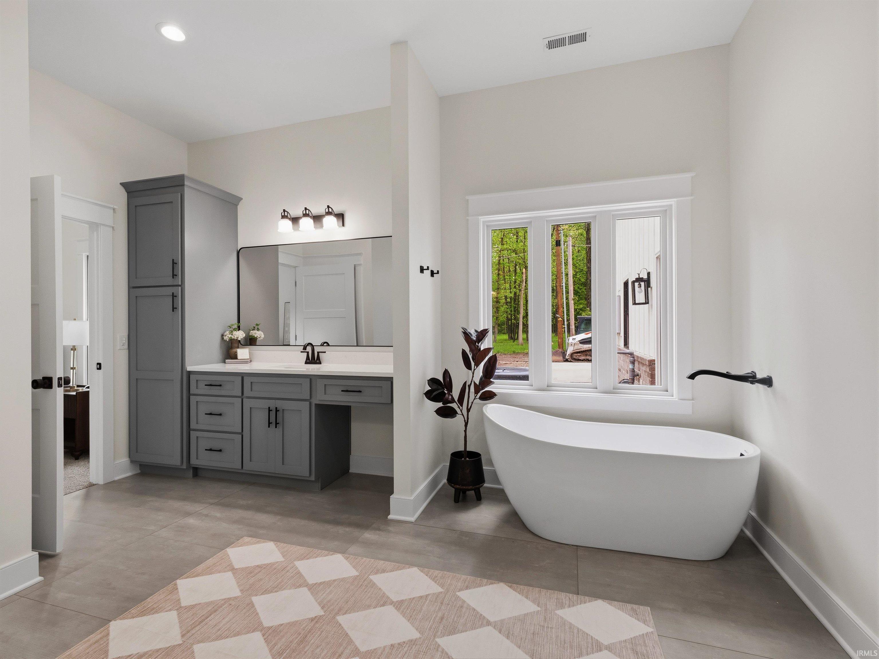 Spacious bathroom featuring a freestanding soaking tub, a large window, a double vanity with ample cabinetry, and a walk-in shower