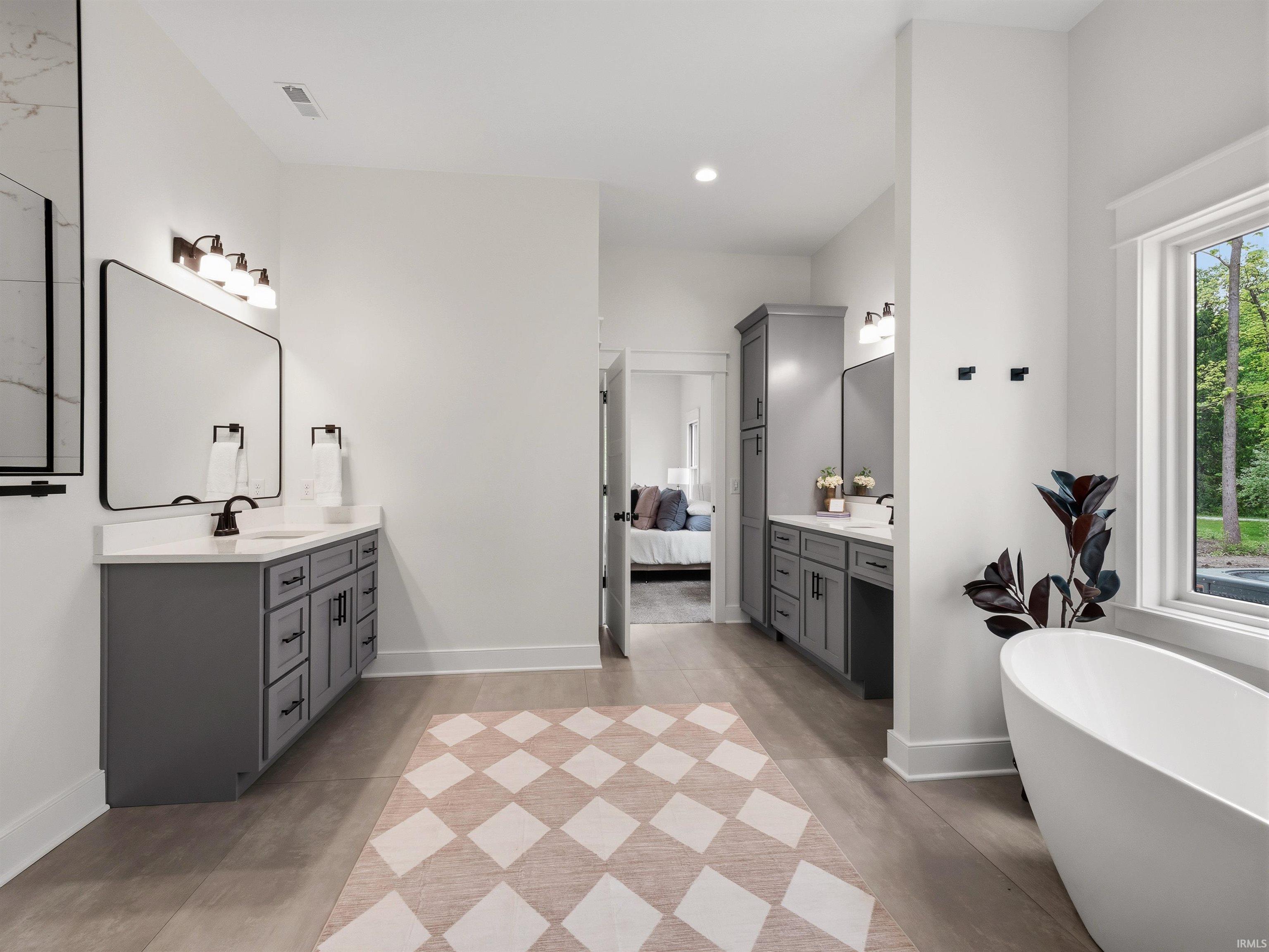 Spacious bathroom featuring two separate vanities with grey cabinetry, white countertops, and black fixtures