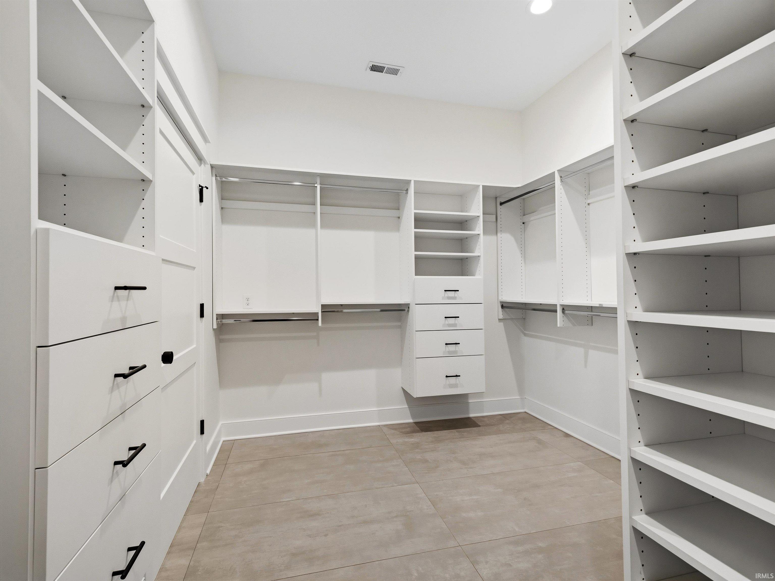 Custom closet system featuring white built-in shelving, multiple hanging rods, integrated drawers with dark hardware, and durable tile flooring