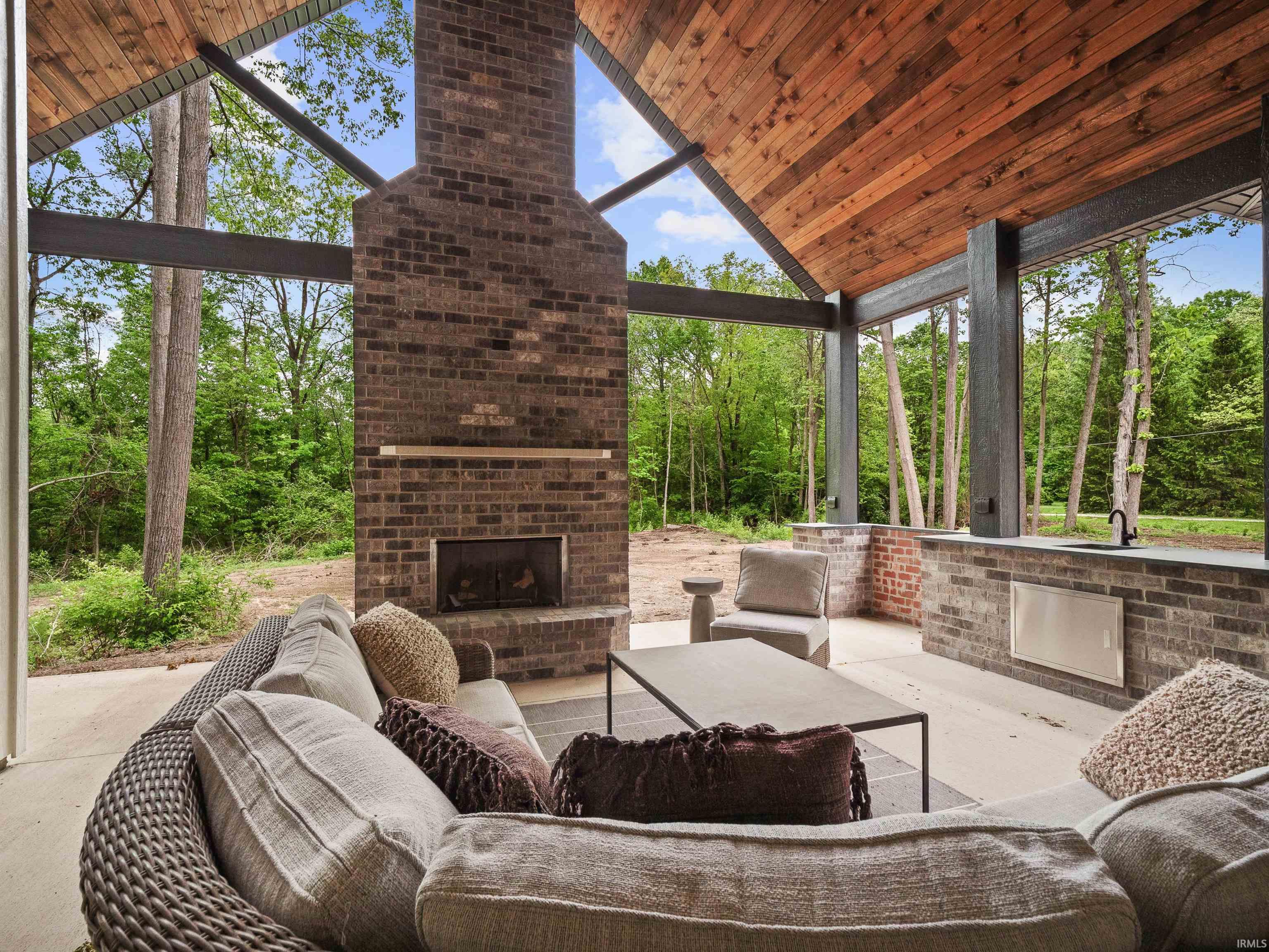 Expansive covered patio featuring a soaring wood-paneled ceiling, a brick fireplace with a hearth, and an integrated outdoor kitchen with a sink and built-in appliance