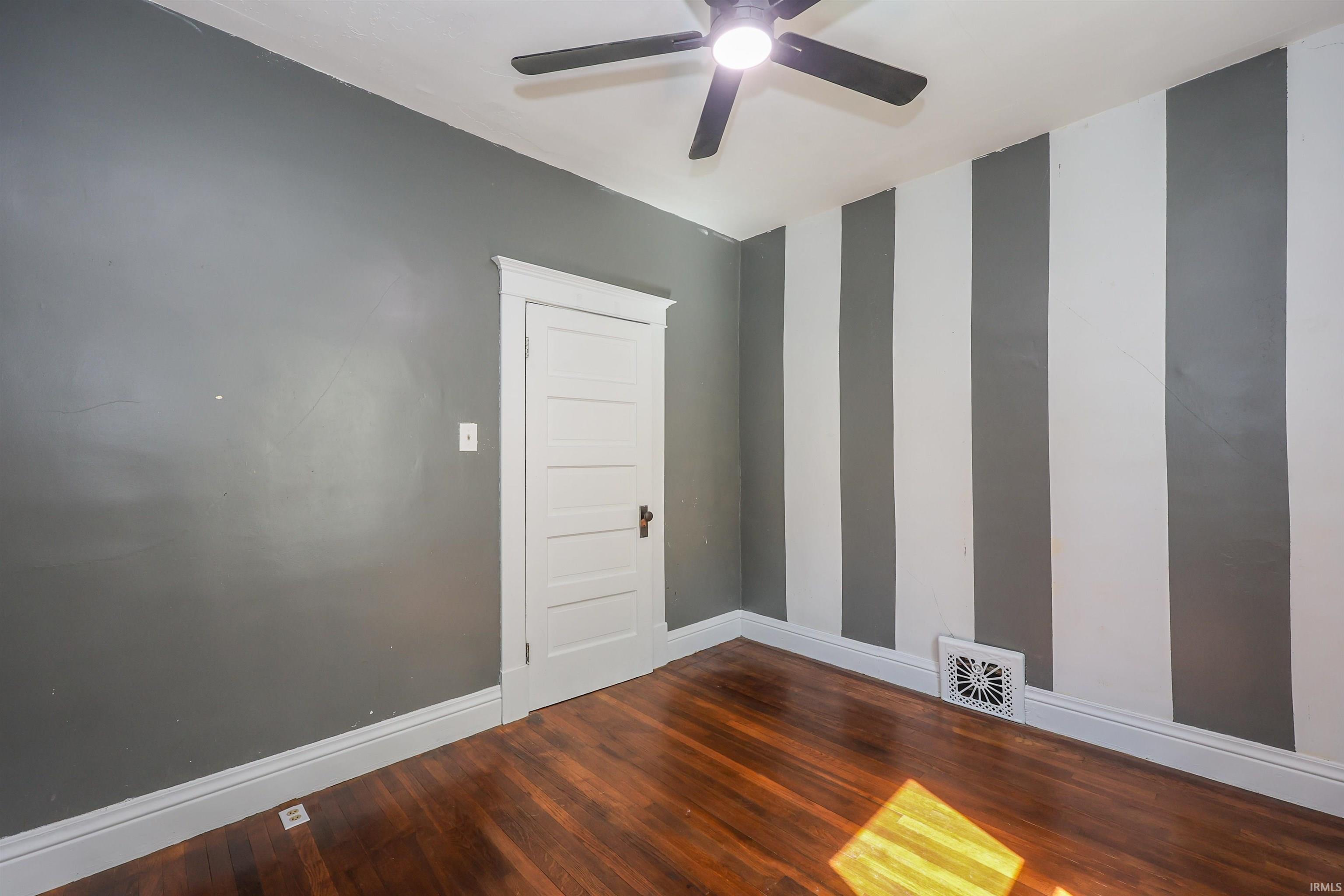 Room featuring wood-finish flooring, a ceiling fan with integrated lighting, and a white paneled door with traditional trim