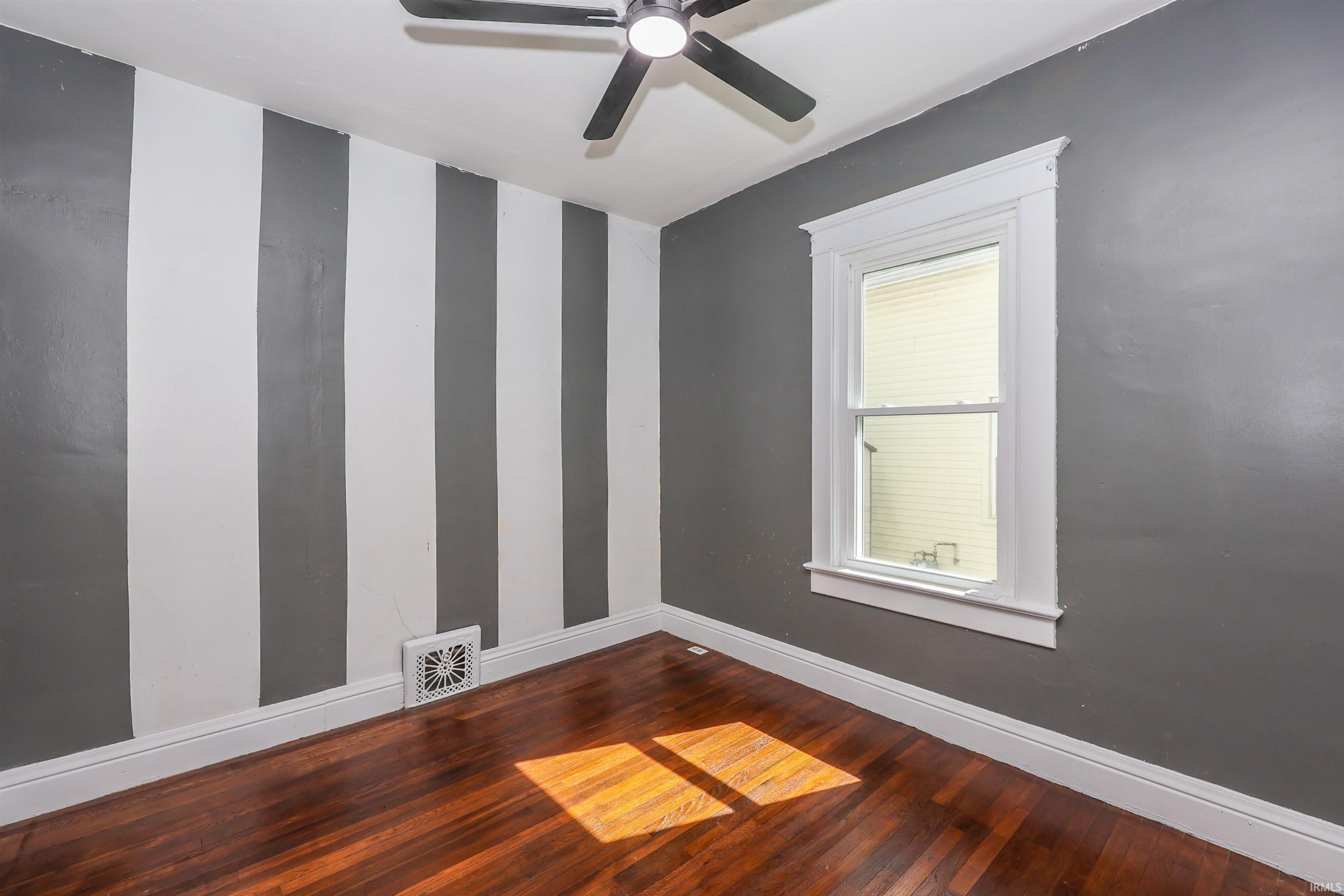 Bright room featuring wood-finish flooring, a ceiling fan, and white trim