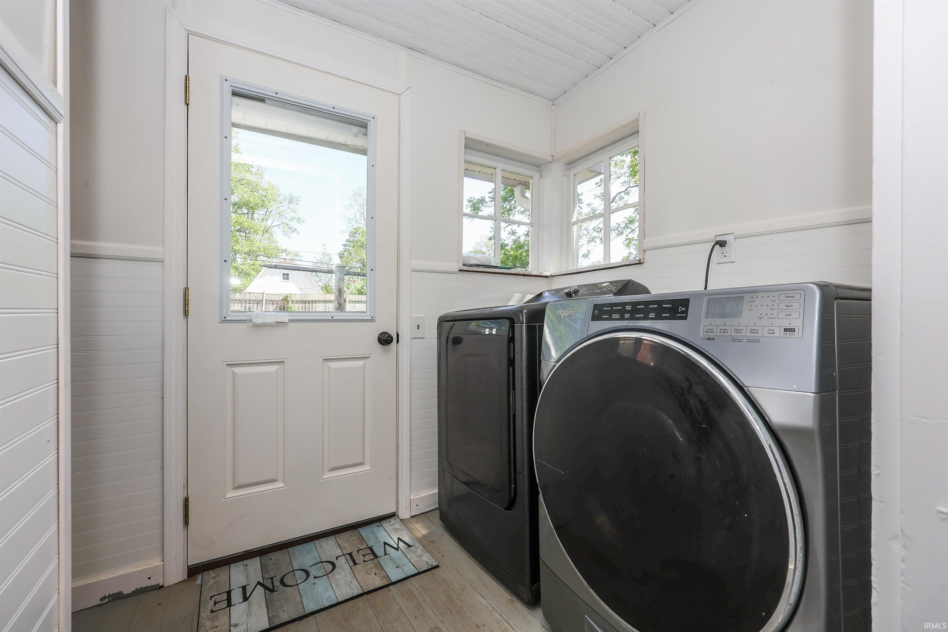 Dedicated laundry area featuring a full-light panel door, corner windows, and beadboard paneling