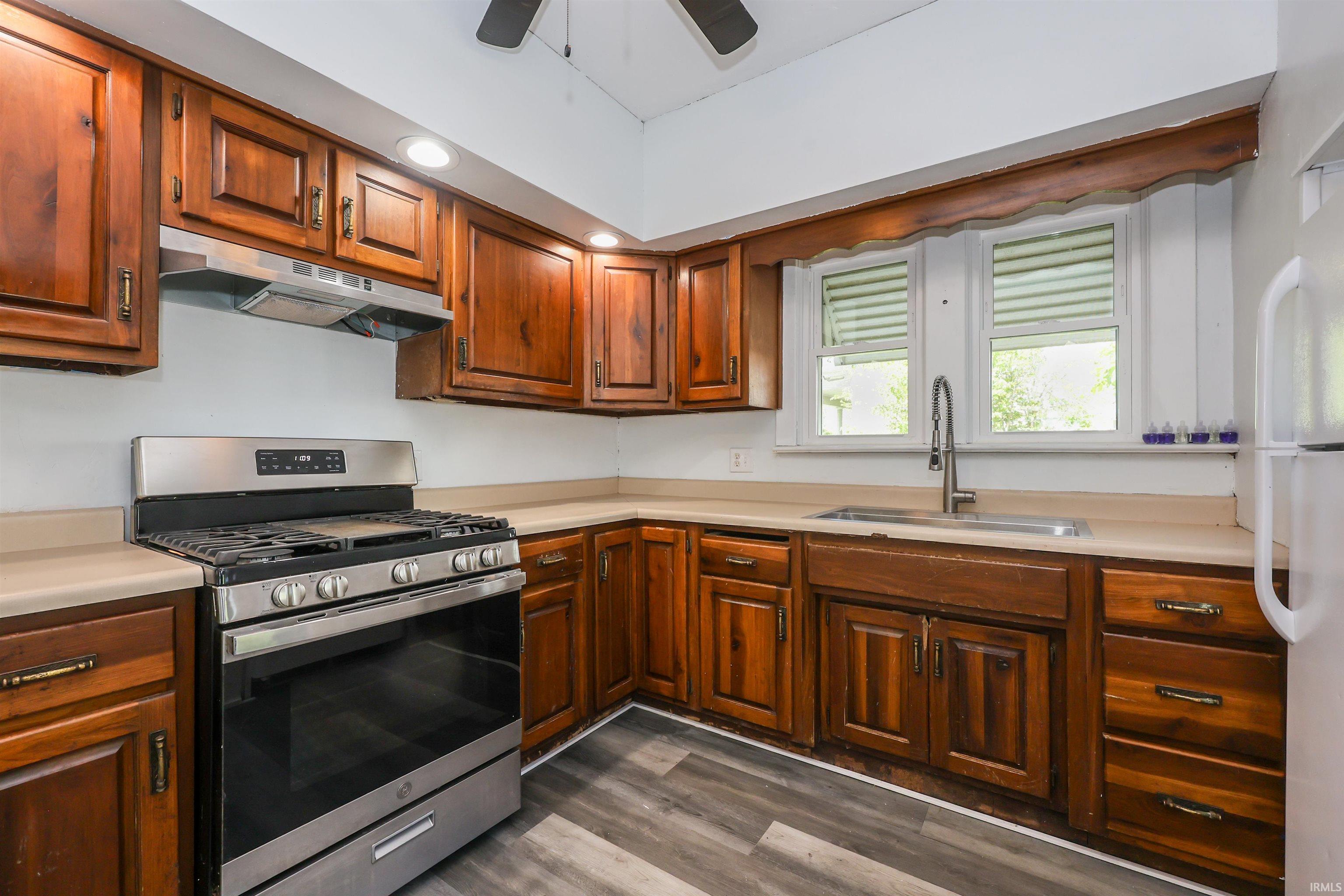 Kitchen featuring wood cabinetry, stainless steel range with overhead ventilation, and a double window above the sink