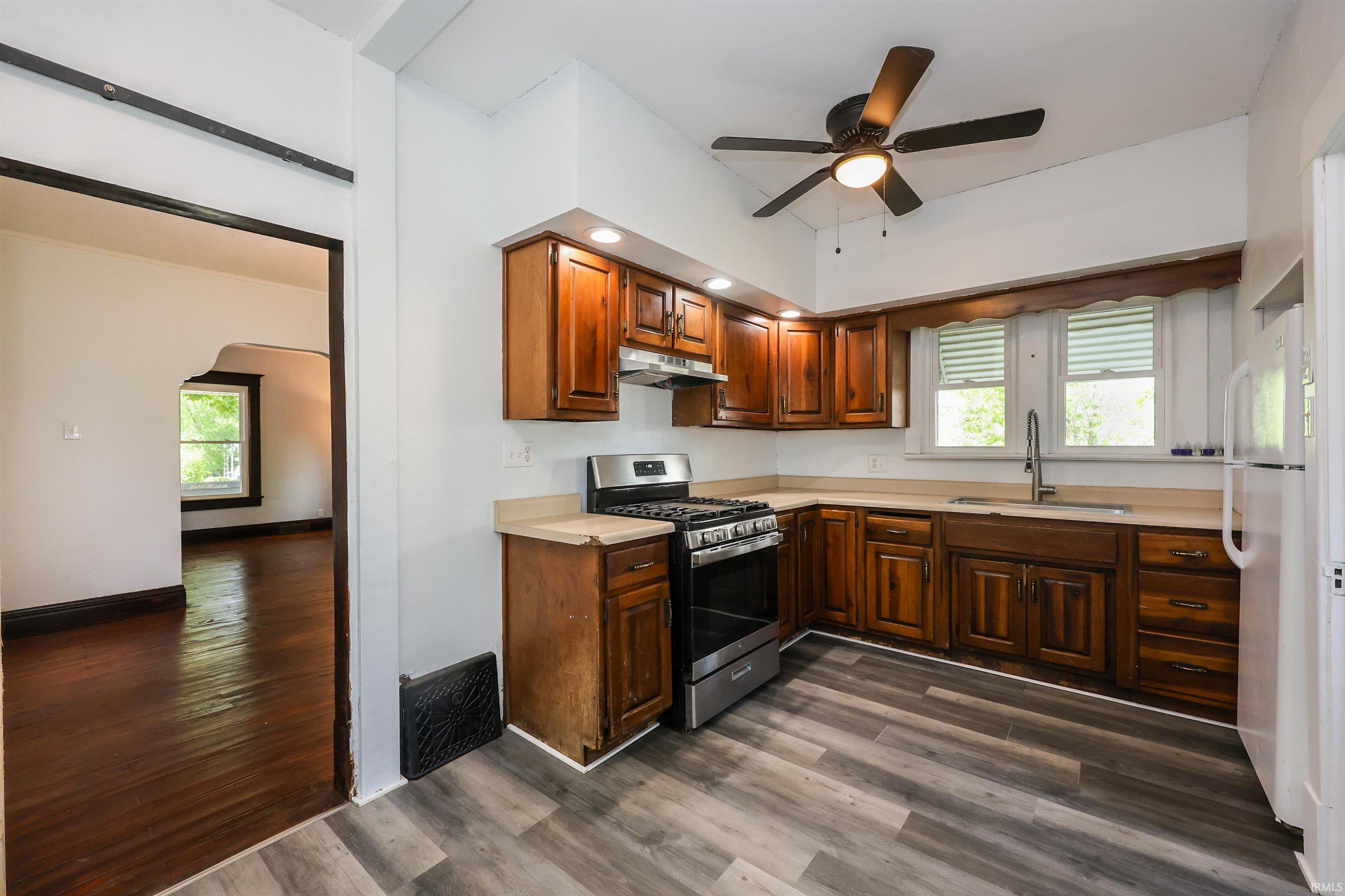 Kitchen featuring wood-finish cabinetry, light-toned countertops, a stainless steel gas range, and a ceiling fan with integrated lighting