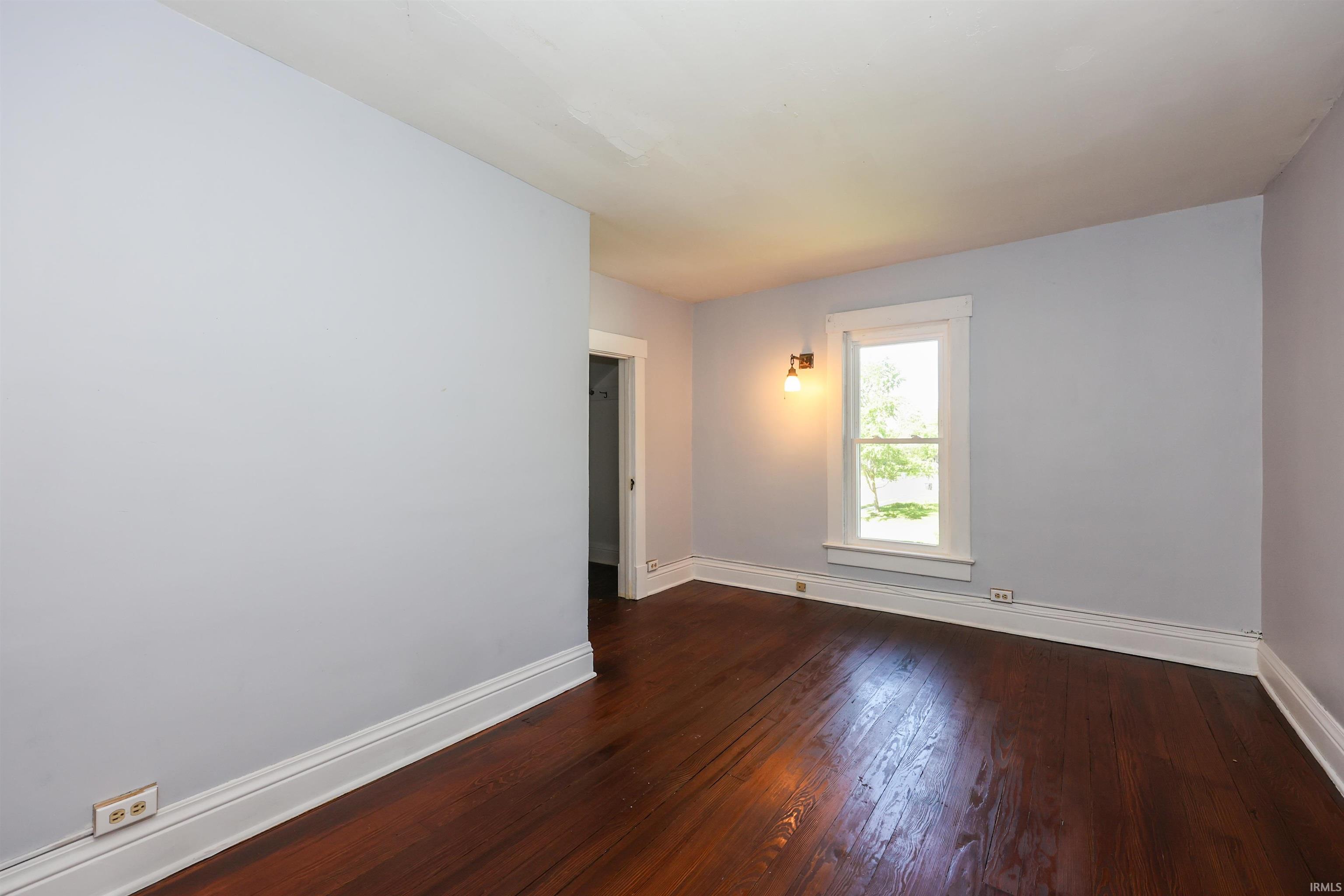 Room featuring wood flooring, white trim, a window with exterior views, and a wall-mounted light fixture